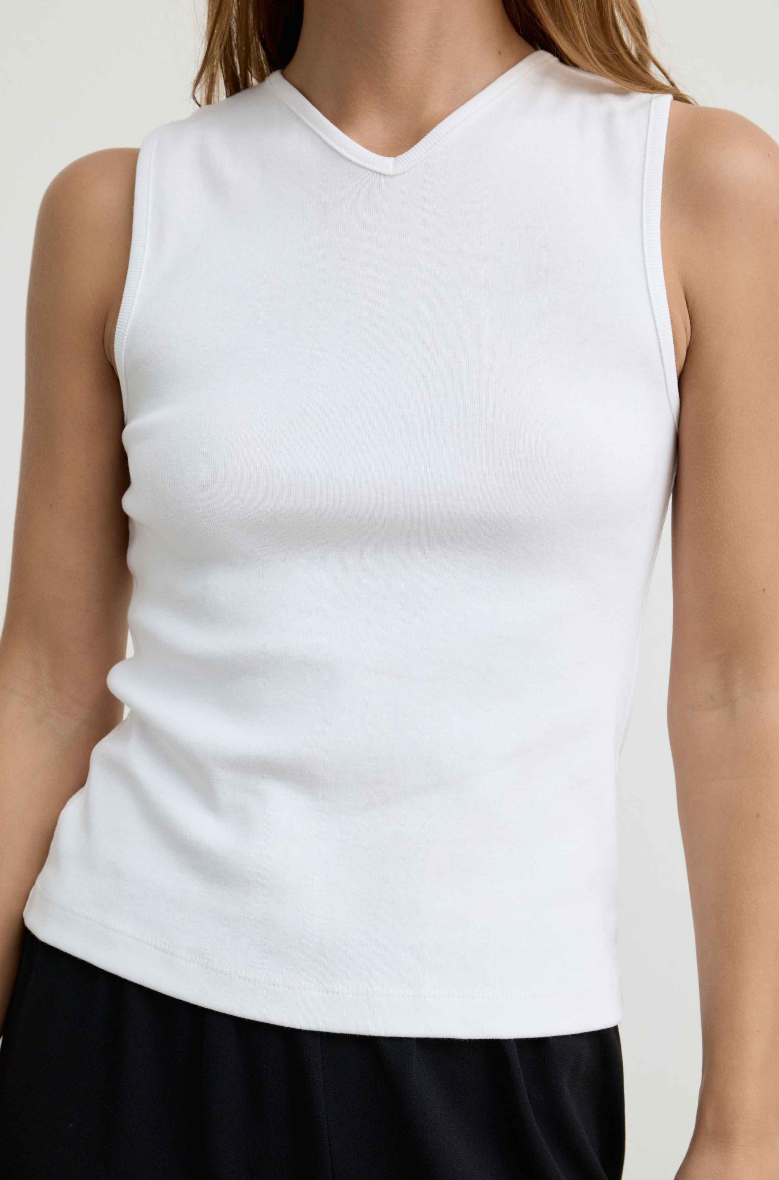 A sleeveless white ribbed knit tank top with a V-neck, shown on a model against a plain light background.