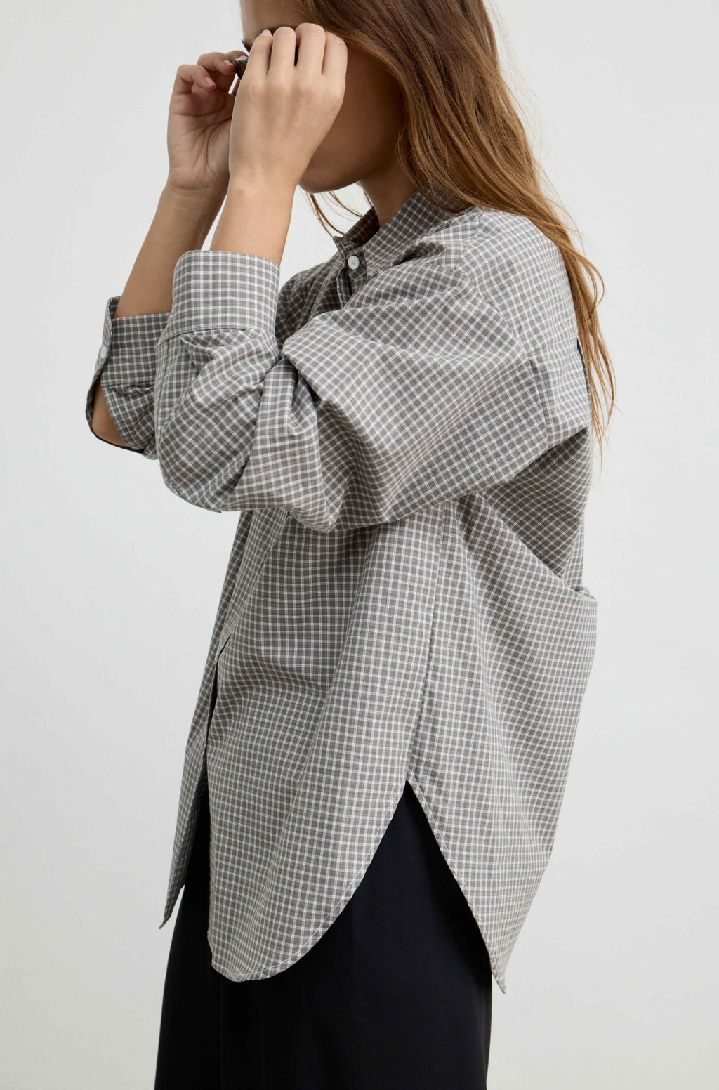 A woman wearing an oversized black and white gingham check button-up shirt with a high-low hem, paired with black bottoms, photographed against a plain light gray background.