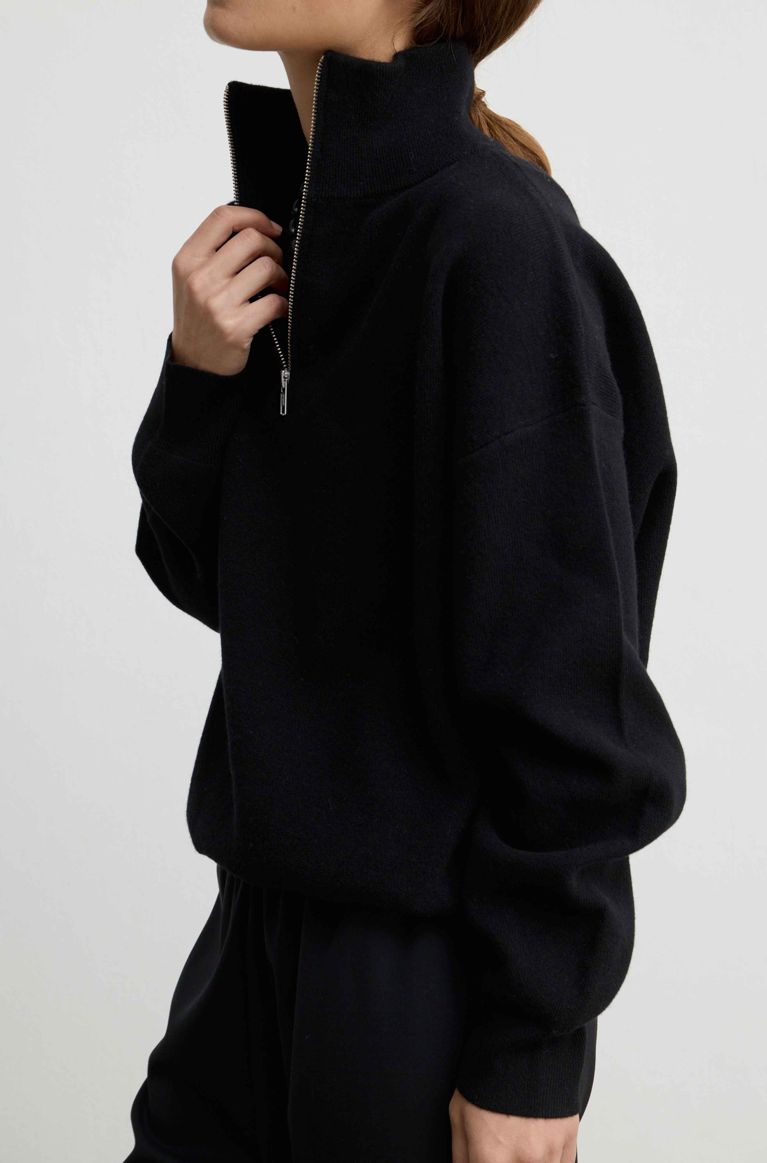 A person wearing a black half-zip mock-neck sweater, shown from the side against a plain light gray studio background.