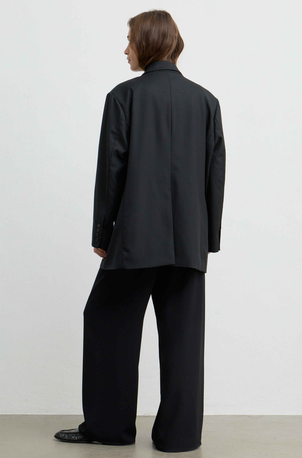 A model shown from the back wearing an oversized black blazer and matching wide-leg trousers against a plain white studio background.