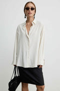 A woman modeling an oversized off-white striped button-up shirt with a black mini skirt and sunglasses, holding a black handbag against a plain light gray background.
