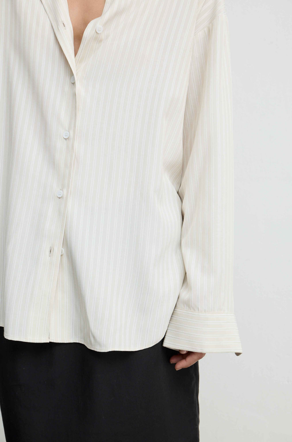 A close-up of a person wearing a cream-colored, long-sleeve button-up shirt with thin vertical stripes, paired with black trousers.