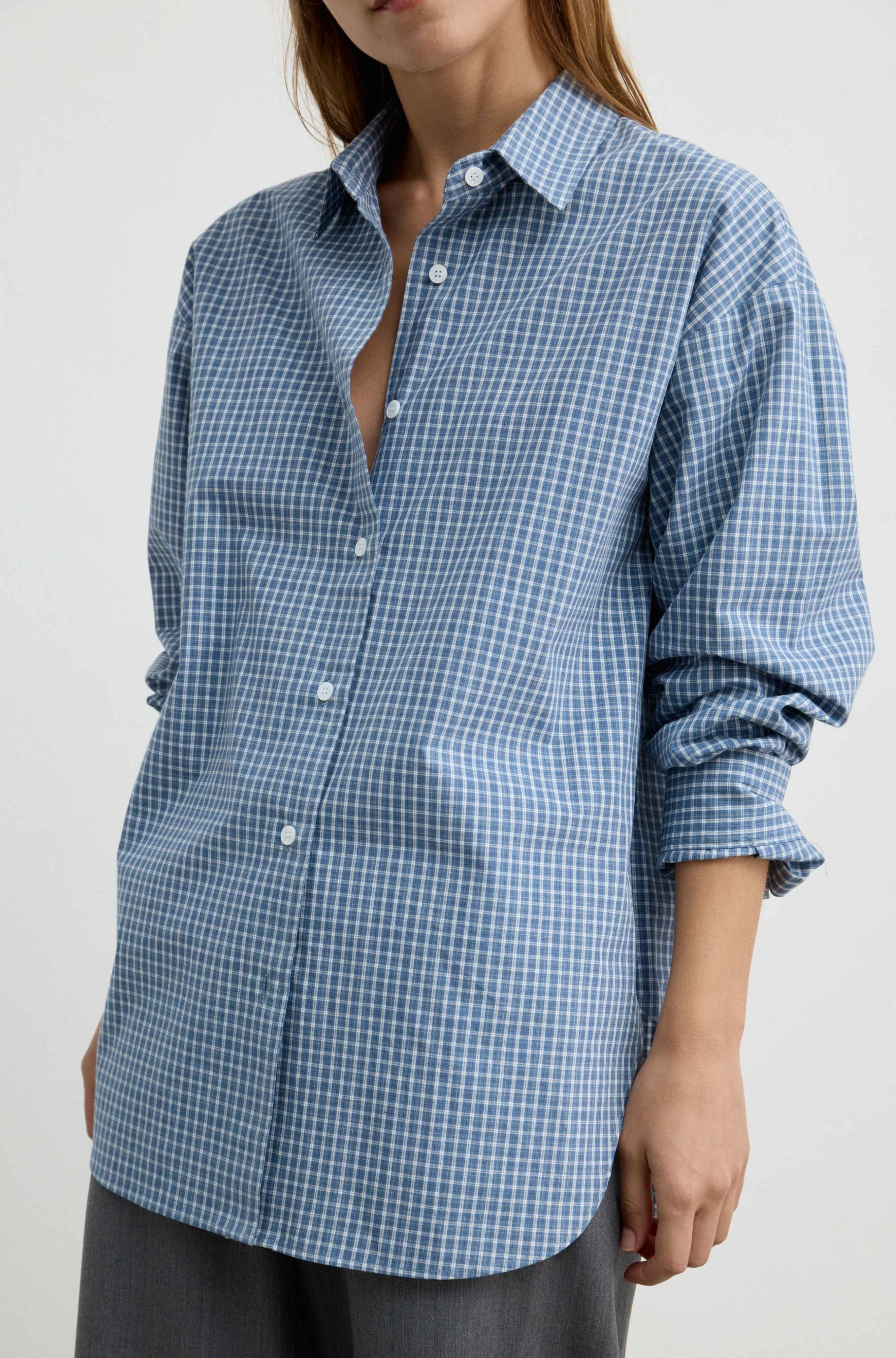 A woman wearing a blue and white gingham check long-sleeve button-up shirt, shown from the neck down against a plain light background.