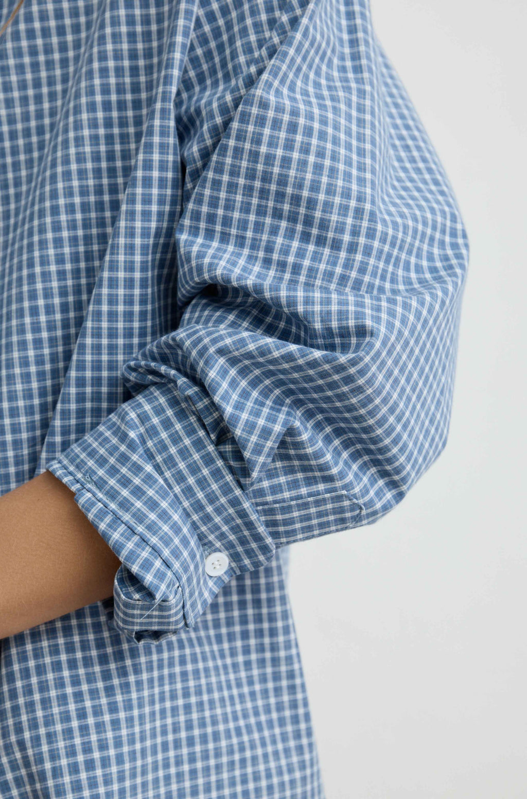 Close-up of a person wearing an oversized blue and white gingham long-sleeve shirt, showing the rolled-up cuff and button.