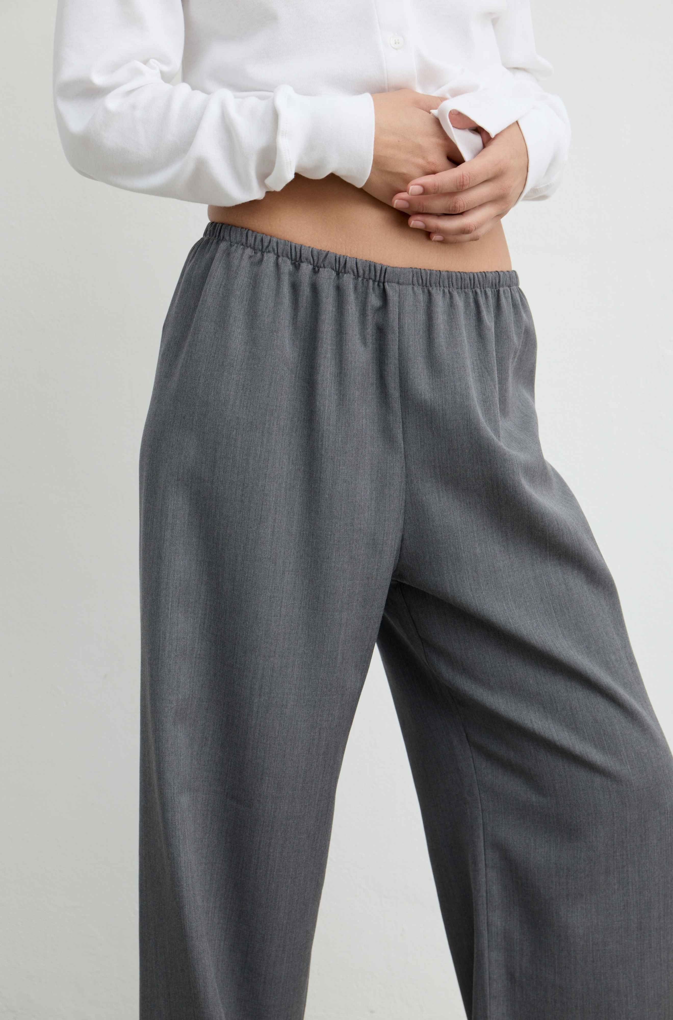 A person wearing loose, wide-leg gray pants with an elastic waistband, paired with a white long-sleeve top, shown from the chest down against a plain light background.