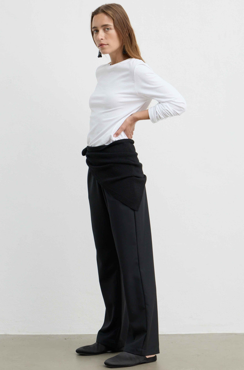 A woman modeling a white long-sleeve top and black wide-leg draped trousers against a plain white studio background.