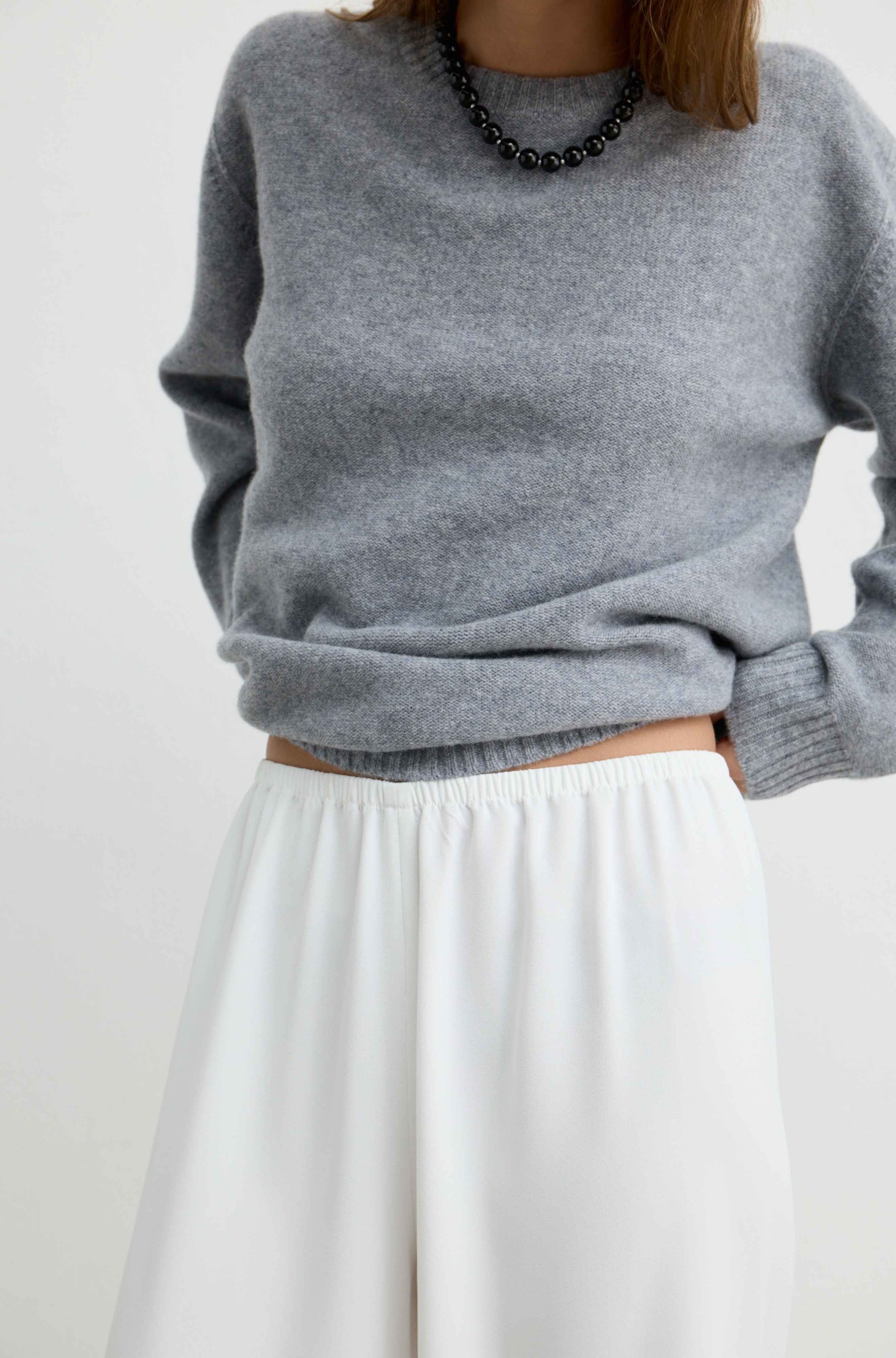 A person wearing a heather gray knit sweater and white wide-leg pants, shown from the neck to the upper thighs against a plain light background.