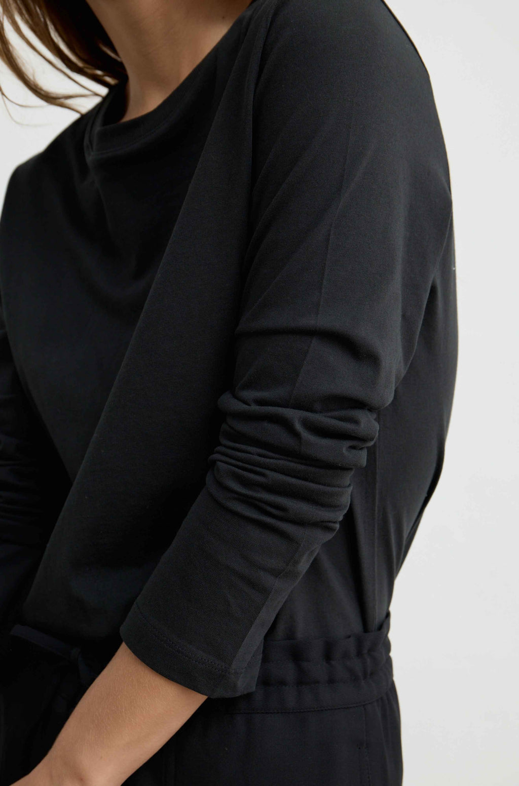 Close-up of a person wearing a black long-sleeve top with gathered sleeves and a drawstring waist, against a plain light background.