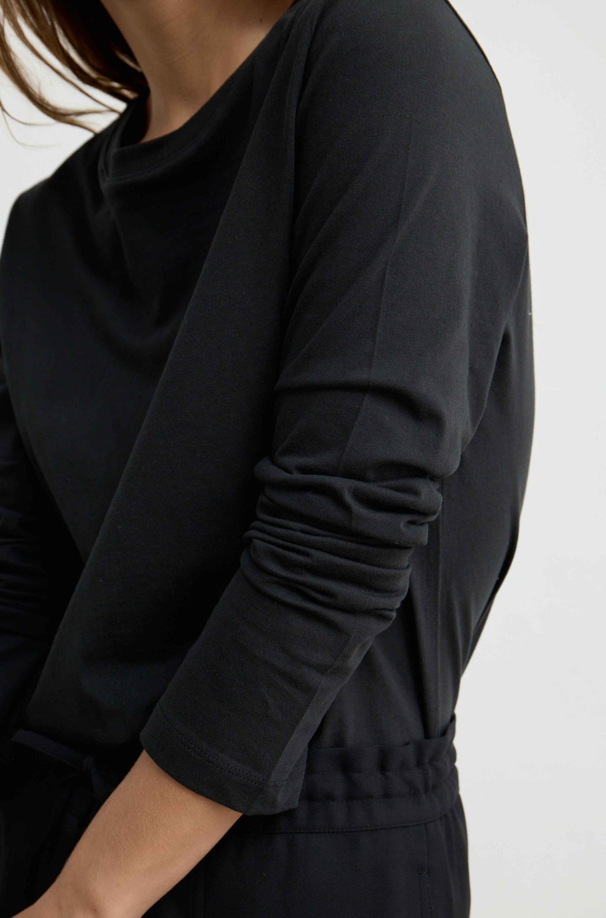 Close-up of a person wearing a black long-sleeve top with gathered sleeves and a drawstring waist, against a plain light background.
