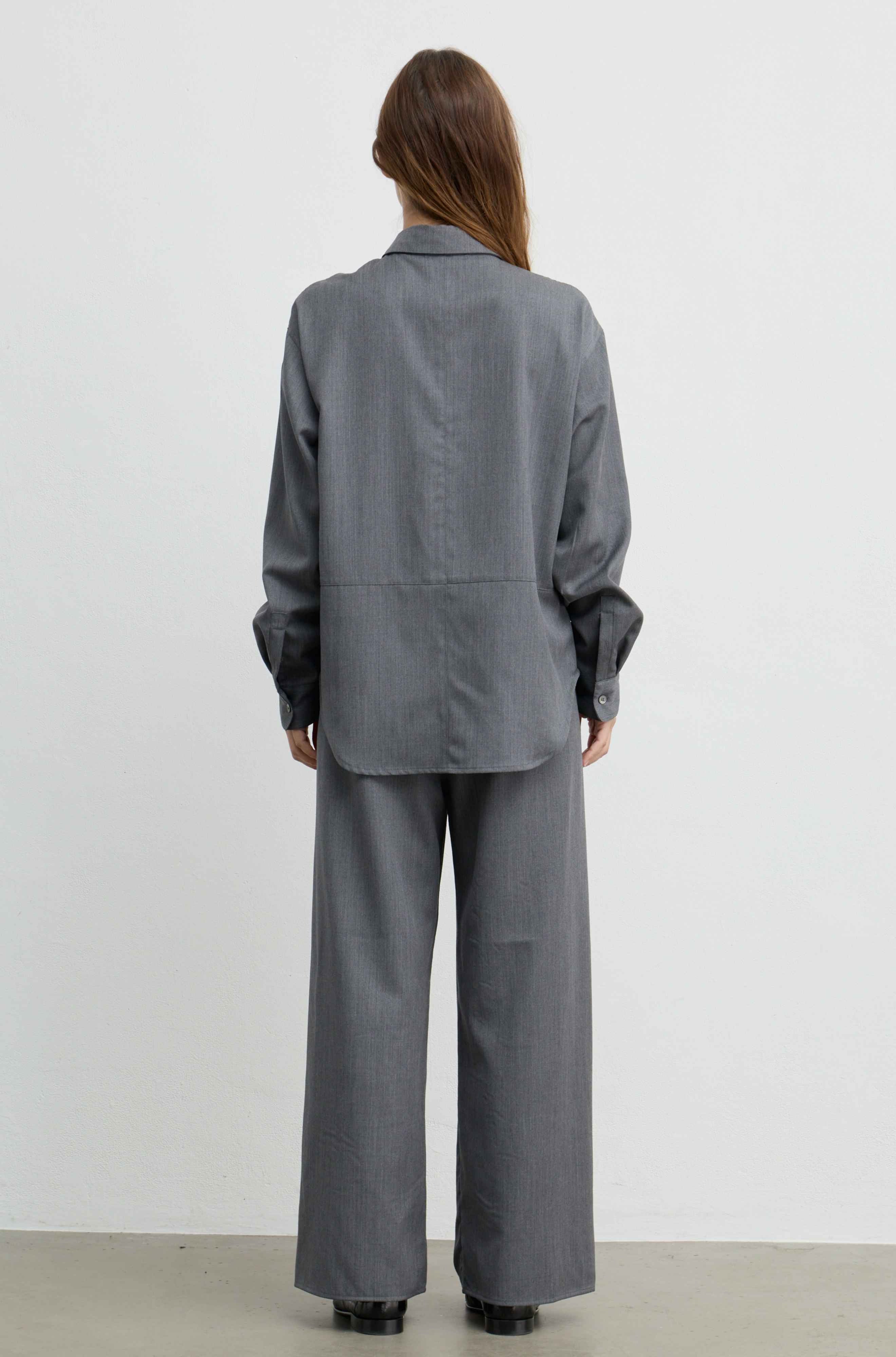 A model viewed from the back wearing a matching gray two-piece suit consisting of a long-sleeve button-down shirt and wide-leg trousers, set against a plain white studio background.