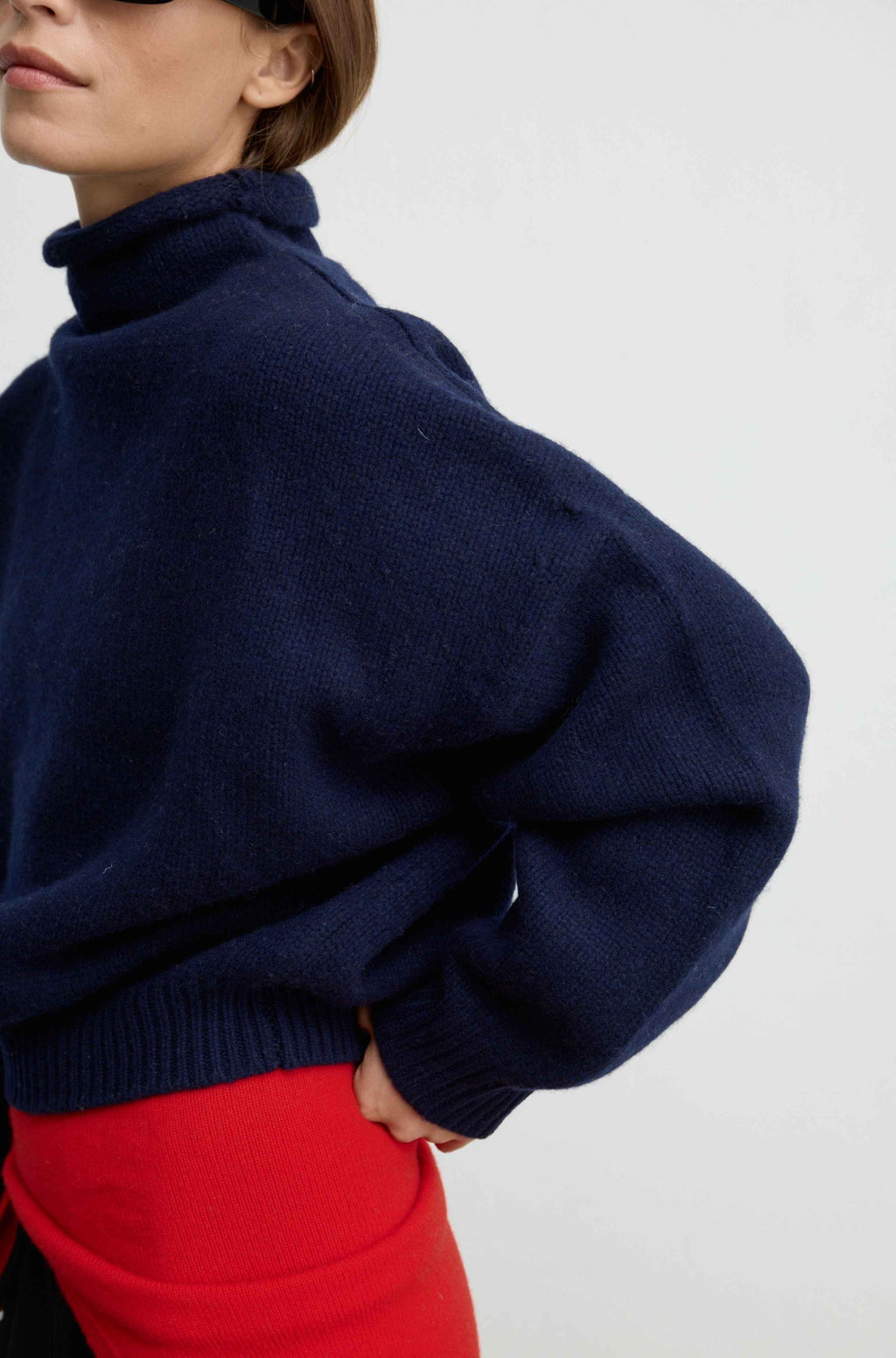 Close up of a woman wearing a navy knit sweater with a mock turtleneck and a red scarf tied around her waist