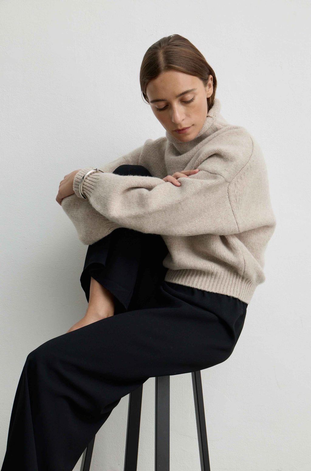 Woman sitting on a chair wearing an oatmeal wool sweater and black pants sitting on a chair