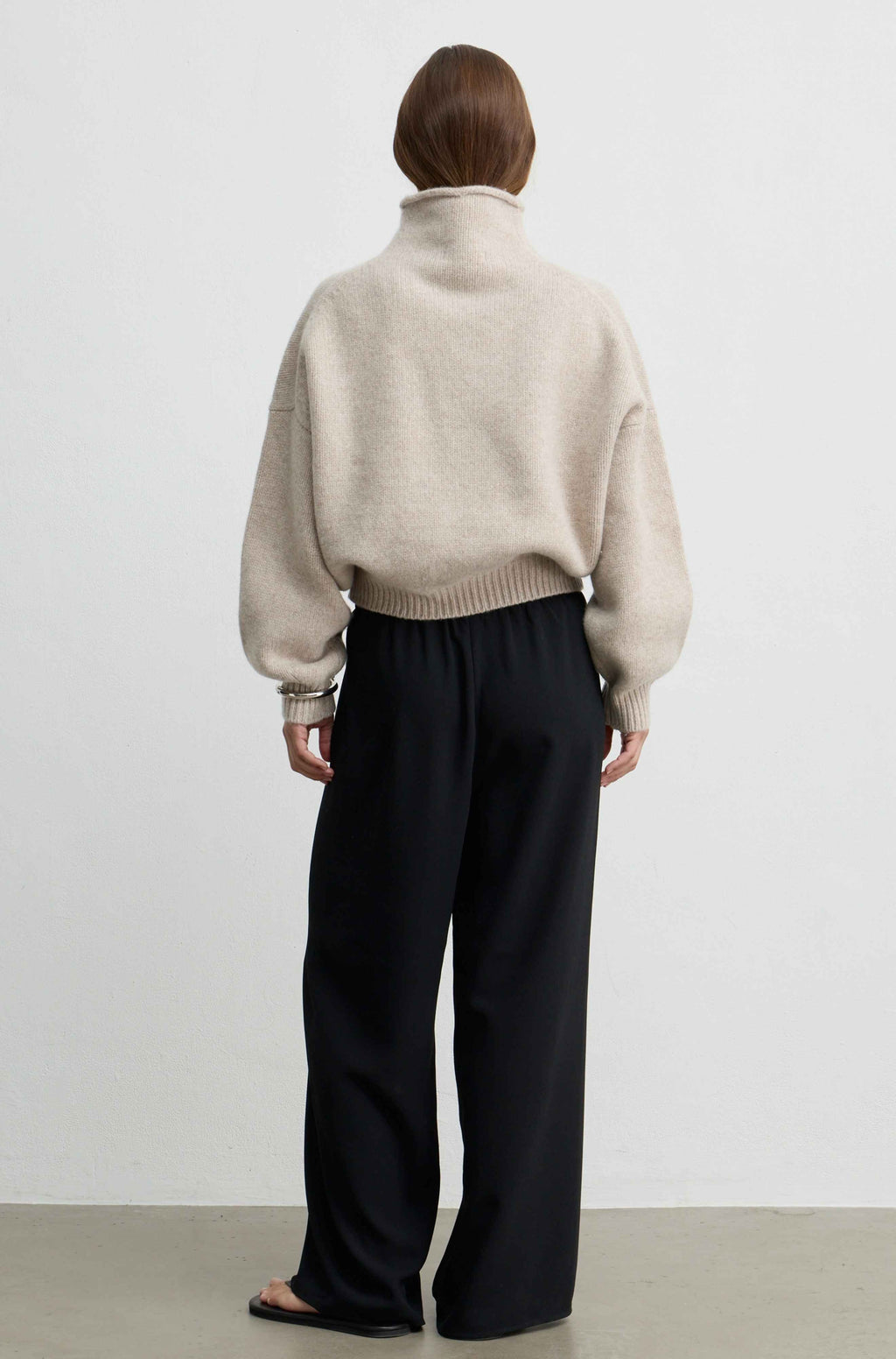Woman wearing a beige wool sweater with black pants against a light grey background