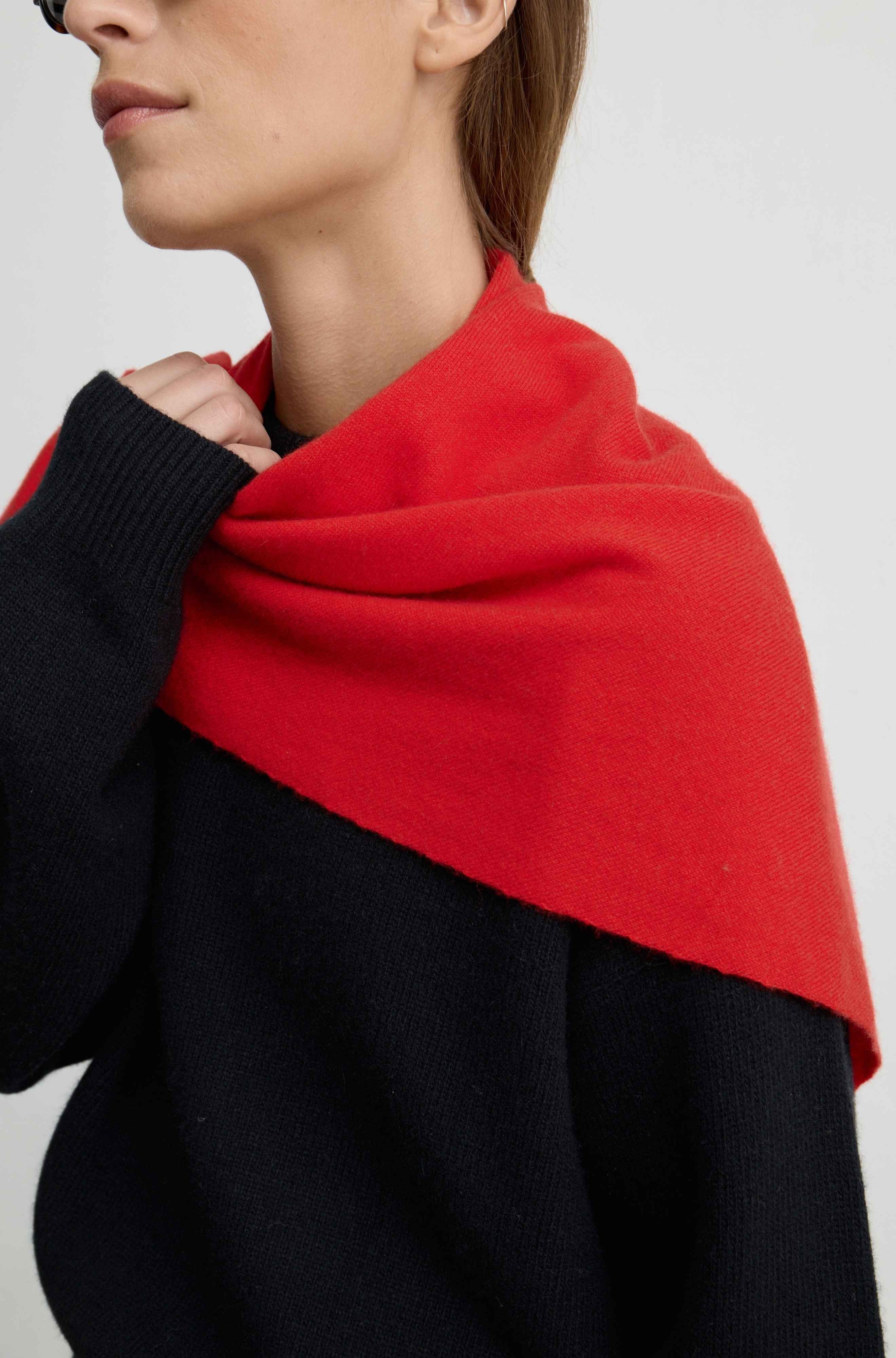 A close-up of a model wearing a color-blocked knit sweater with a vibrant red scarf draped over the shoulders.