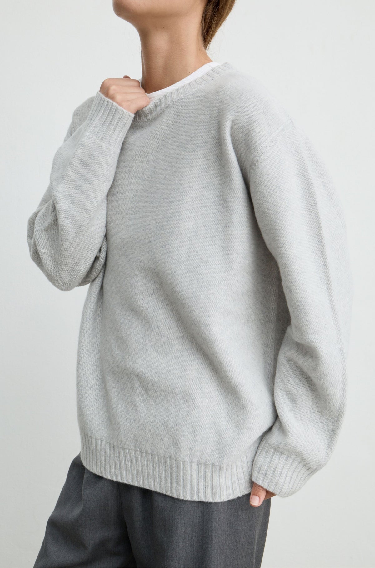 A person wearing an oversized light gray knit sweater with ribbed cuffs and hem, paired with dark gray pants, photographed against a plain light background.