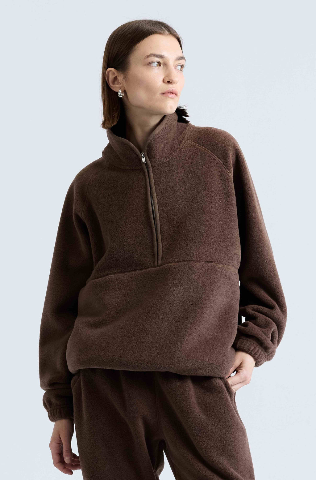 Person wearing a brown fleece pullover with a high collar on a light gray background