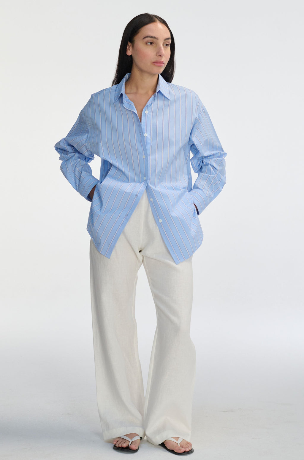 Woman wearing a light blue striped shirt and white pants on a white background