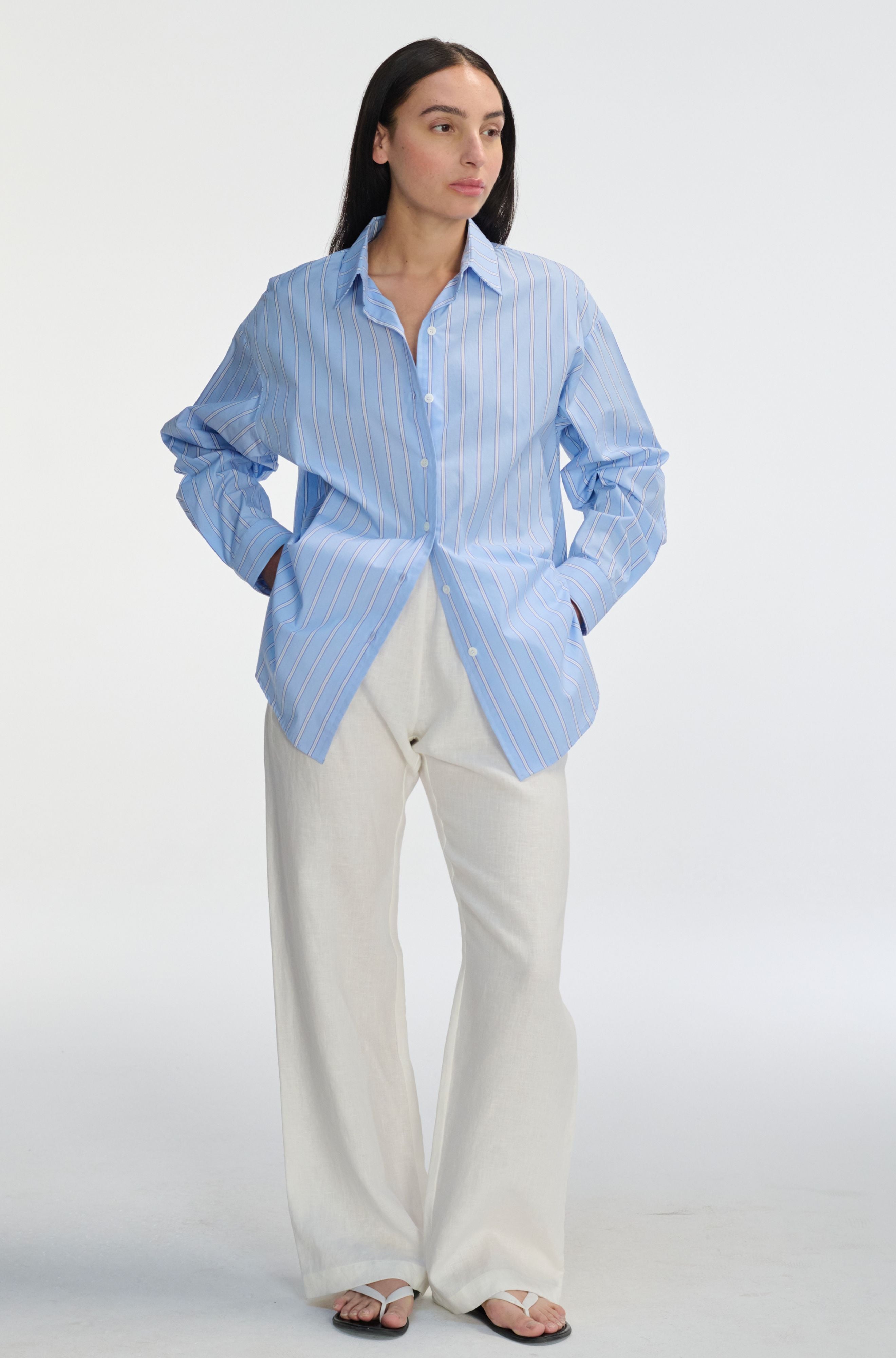 Woman wearing a light blue striped shirt and white pants on a white background