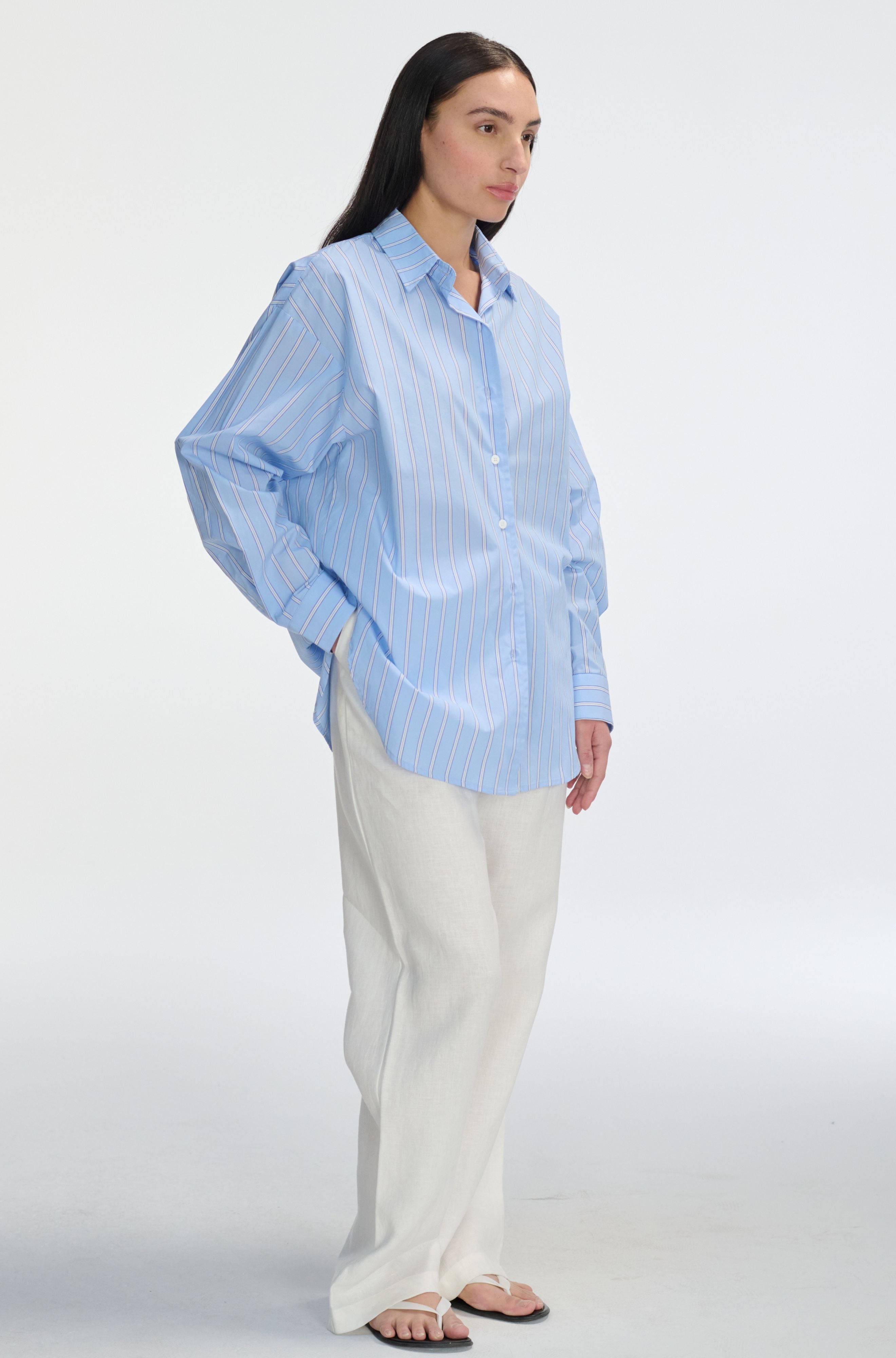 Woman wearing a light blue striped shirt and white pants on a white background