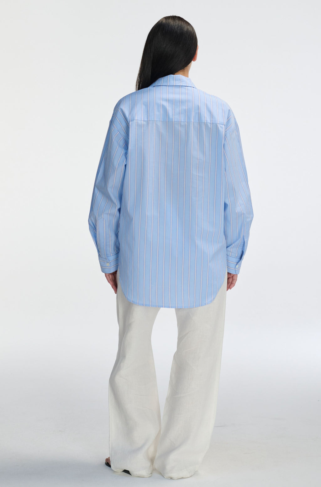 Person wearing a light blue striped shirt and white pants on a white background