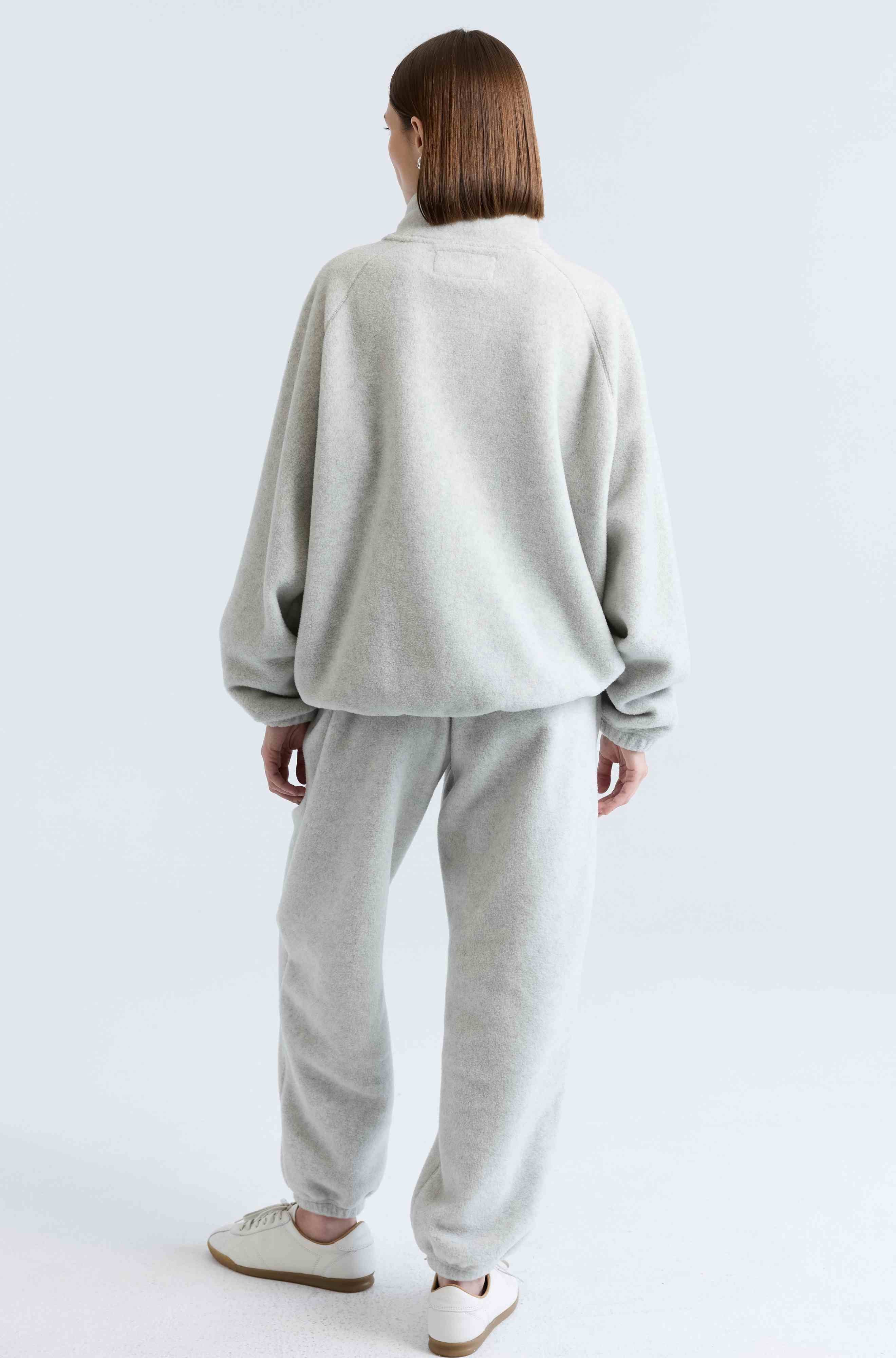 Person wearing a light gray sweatshirt and pants set on a white background