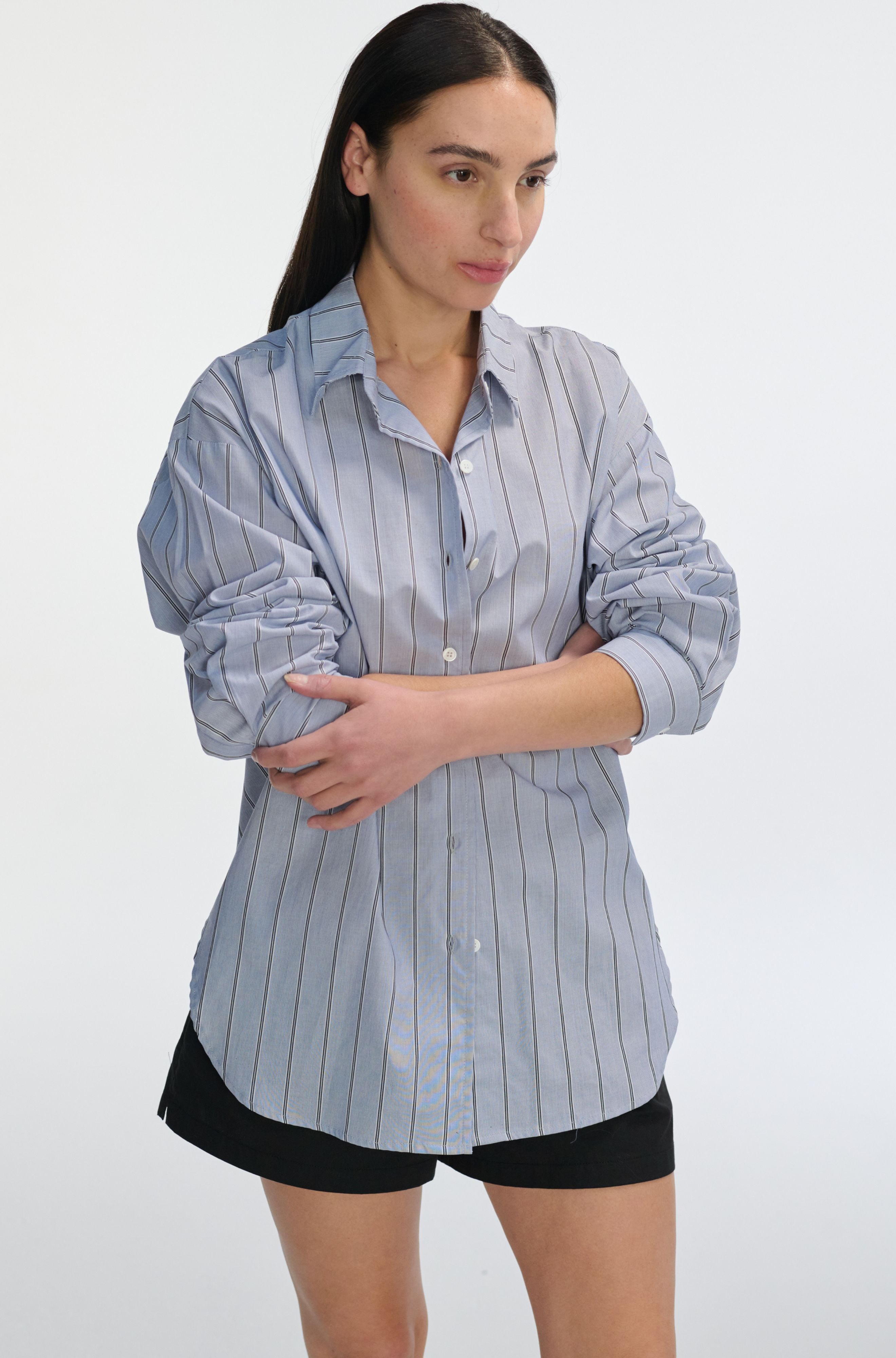 Woman wearing a blue striped shirt and black shorts on a white background