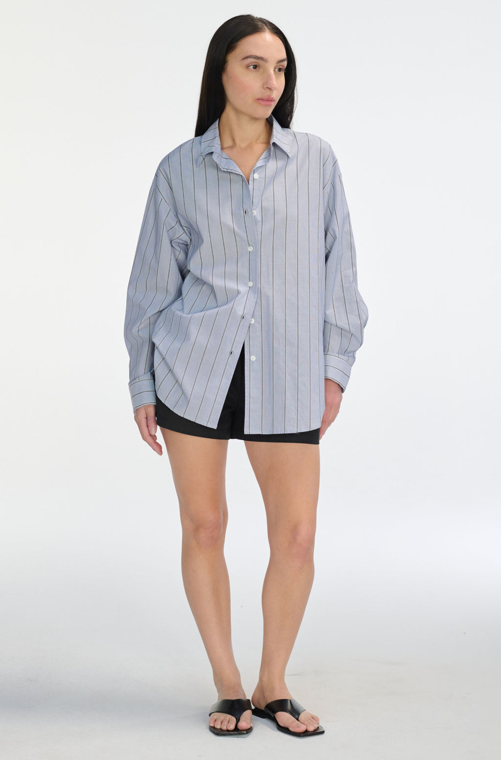 Woman wearing a blue striped shirt over a black top with shorts on a white background