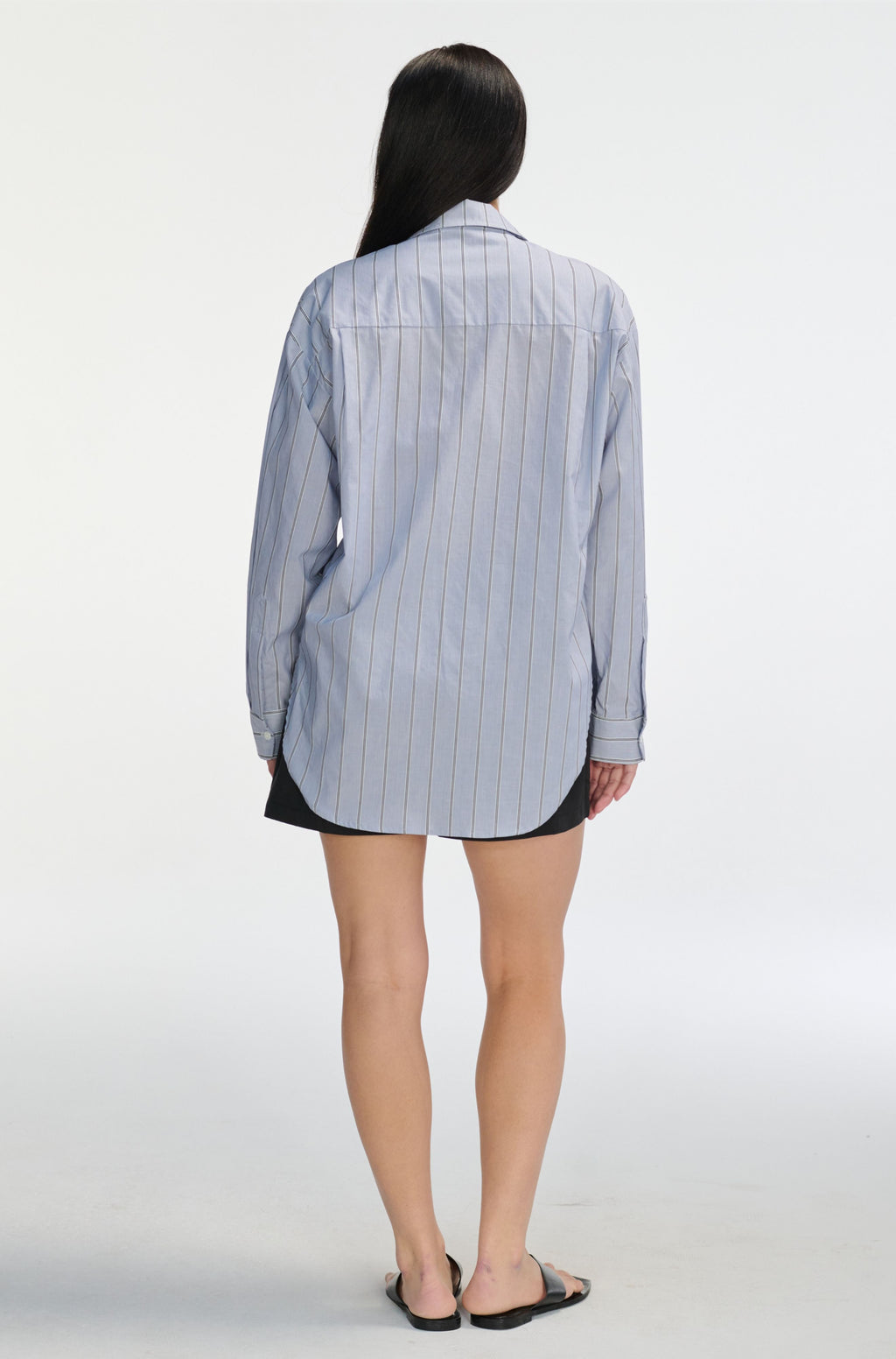 Person wearing a light blue striped shirt over a black skirt on a white background