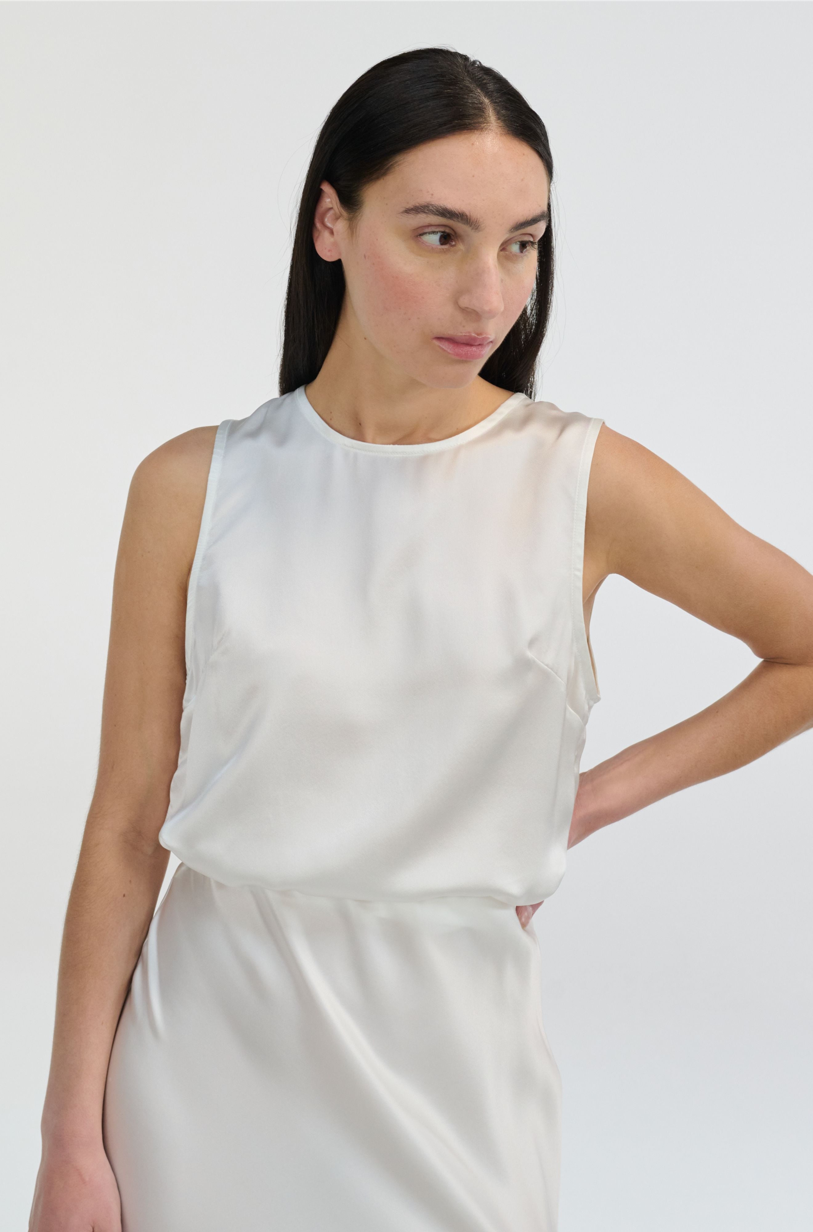 Woman wearing a white sleeveless silk top and matching skirt against a plain background