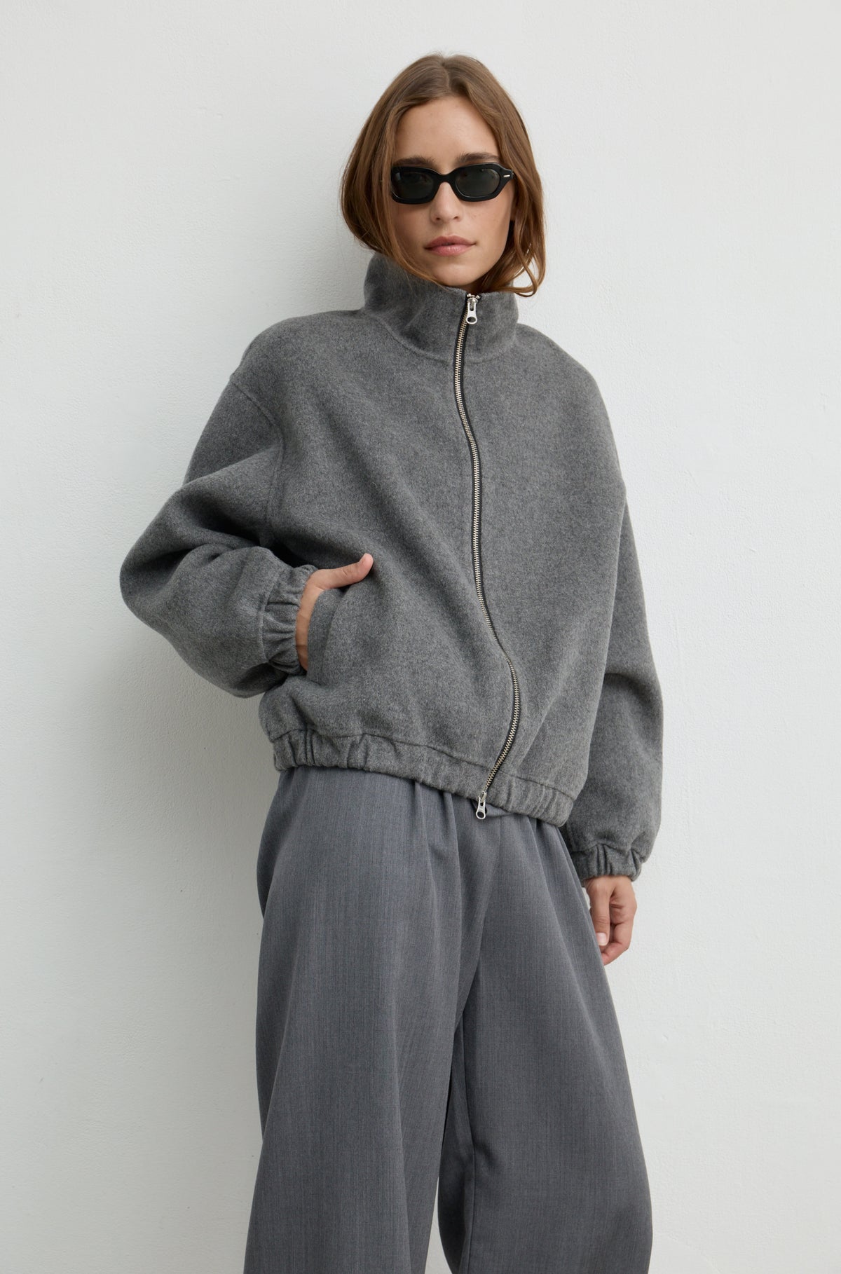 Woman wearing grey wool pants with a grey button up shirt and a wool bomber jacket over