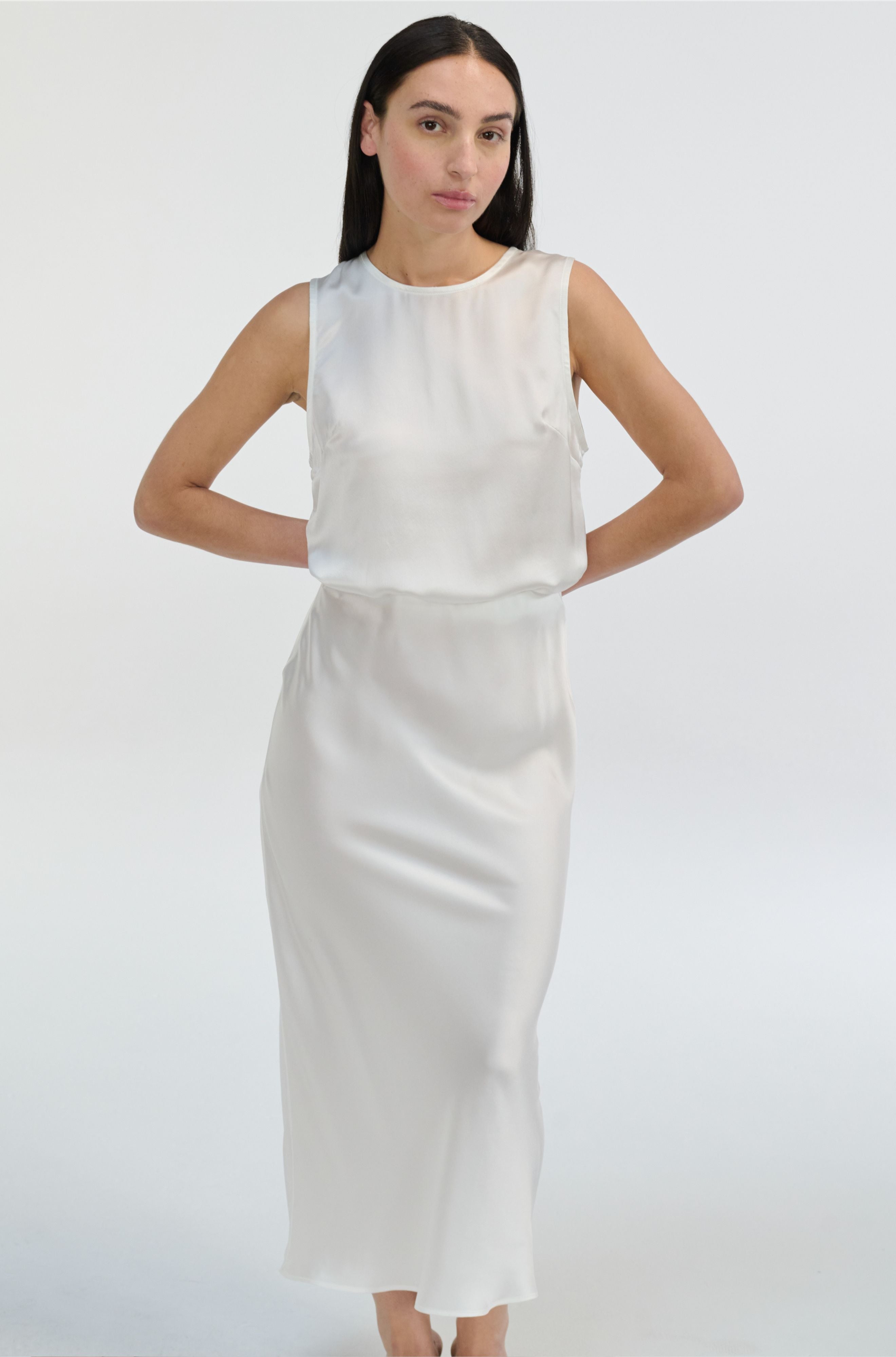 Woman wearing a white sleeveless silk  top and skirt set on a plain background