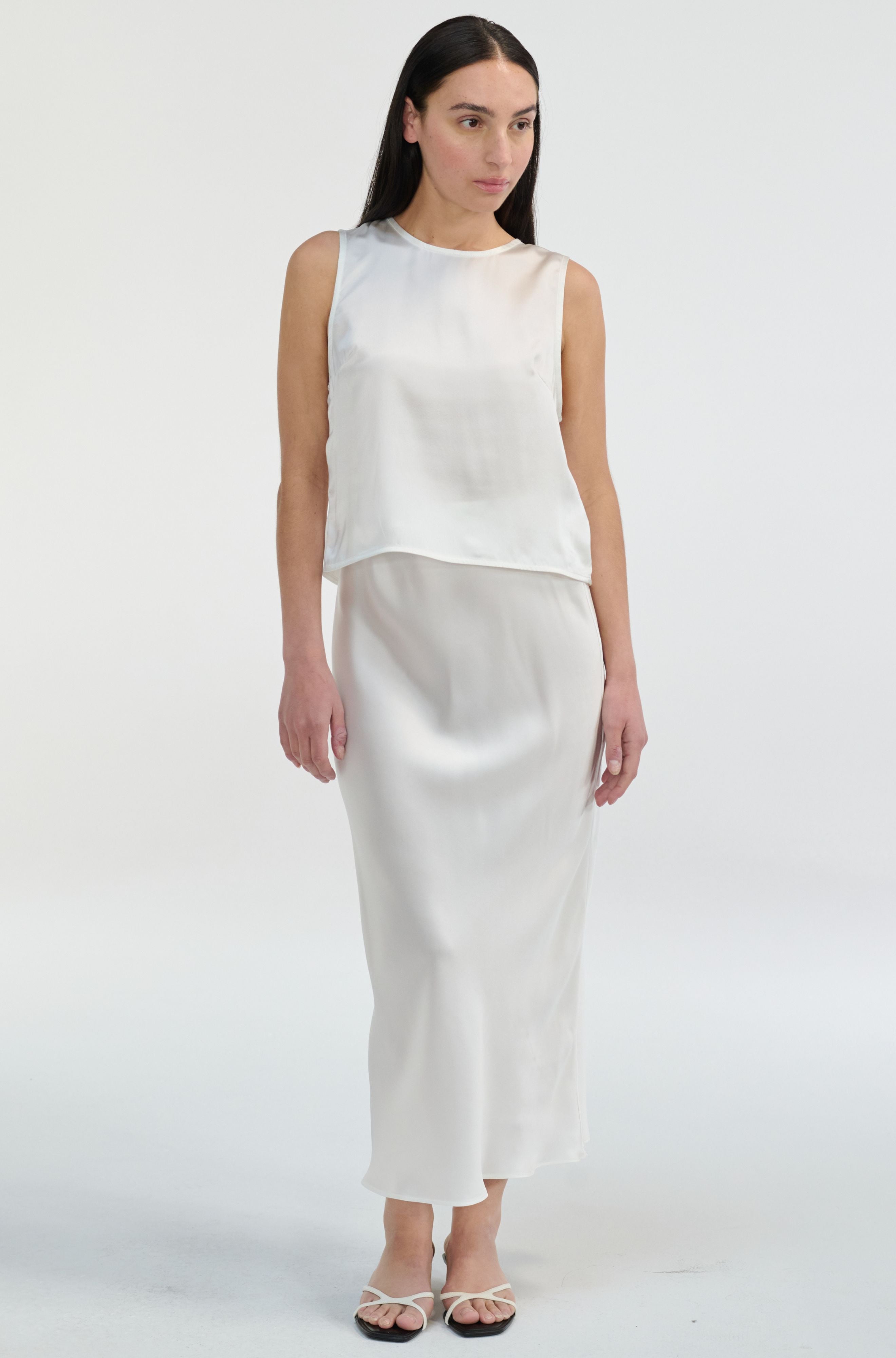 Woman wearing a white sleeveless silk top and skirt on a white background