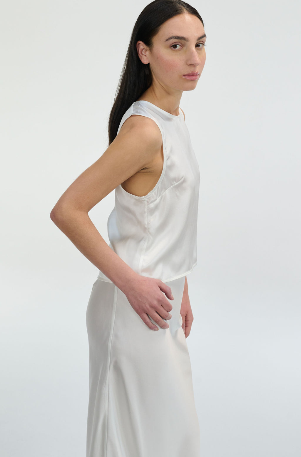Woman wearing a white silk sleeveless top and pants on a plain background