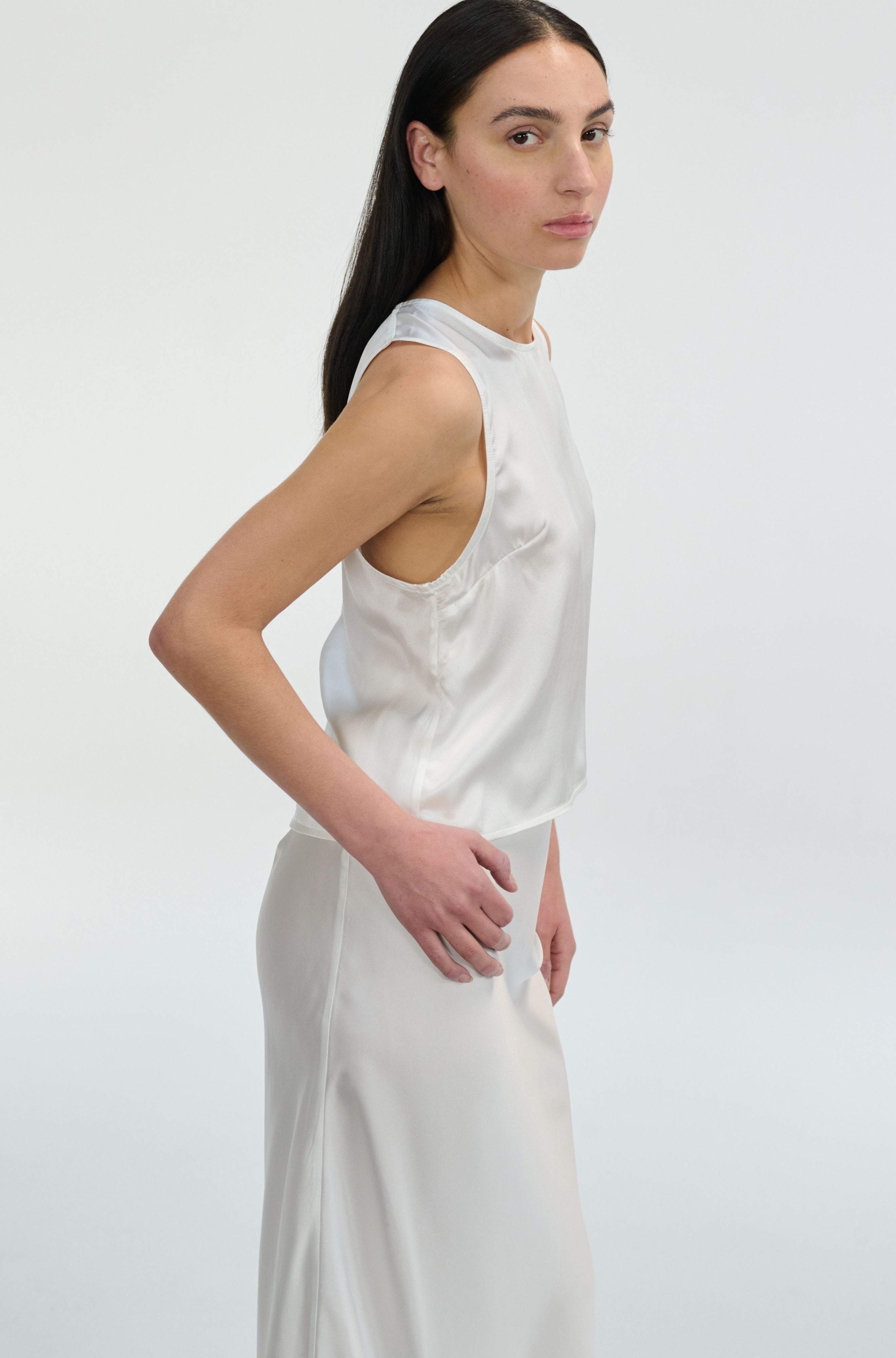 Woman wearing a white silk sleeveless top and pants on a plain background