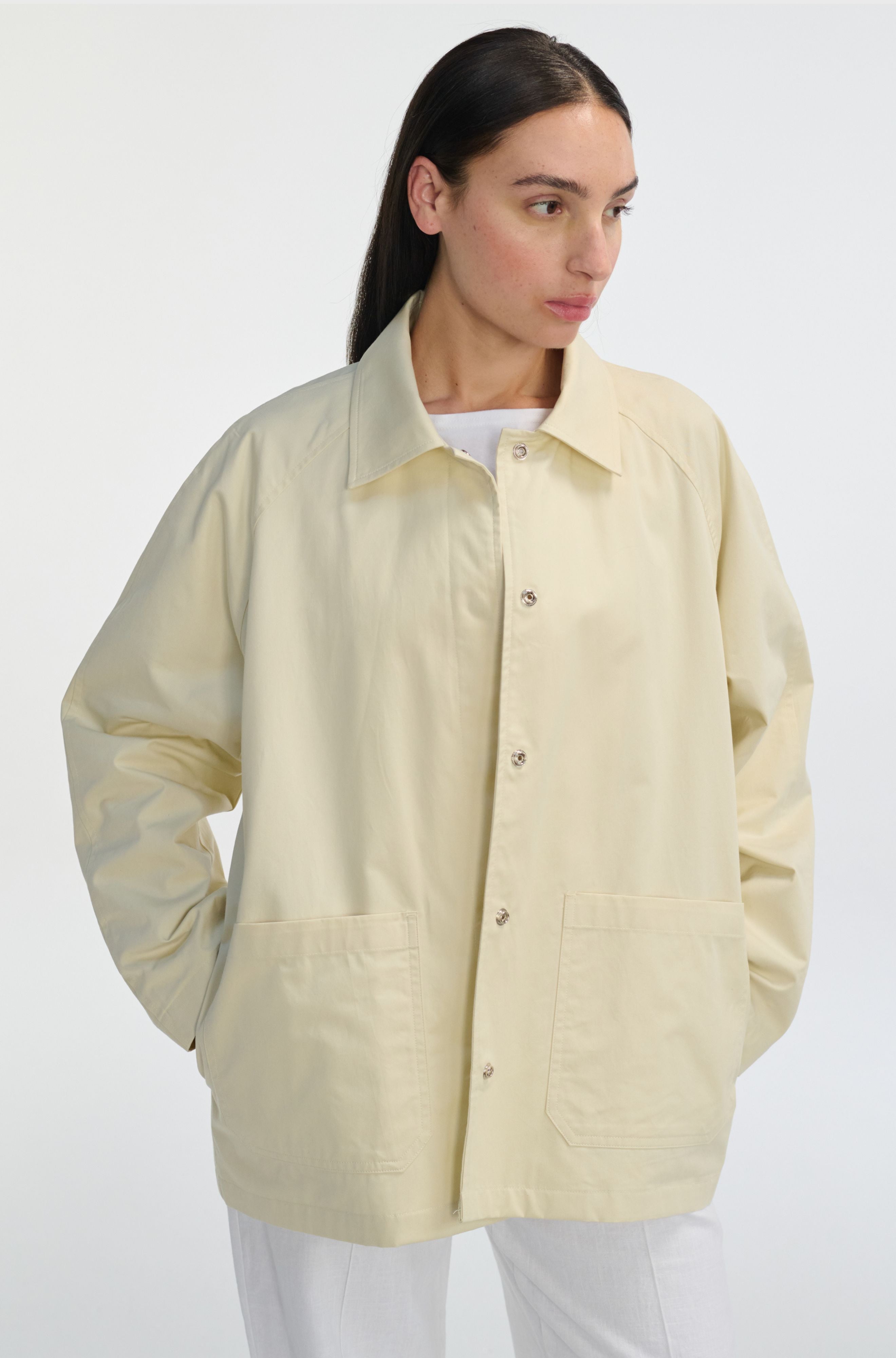 Woman wearing an ivory button up barn jacket with white pants on a white background