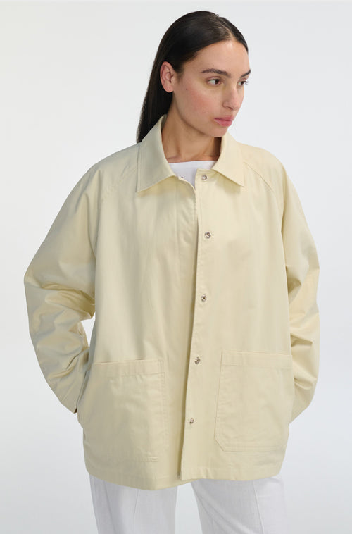 Woman wearing an ivory button up barn jacket with white pants on a white background