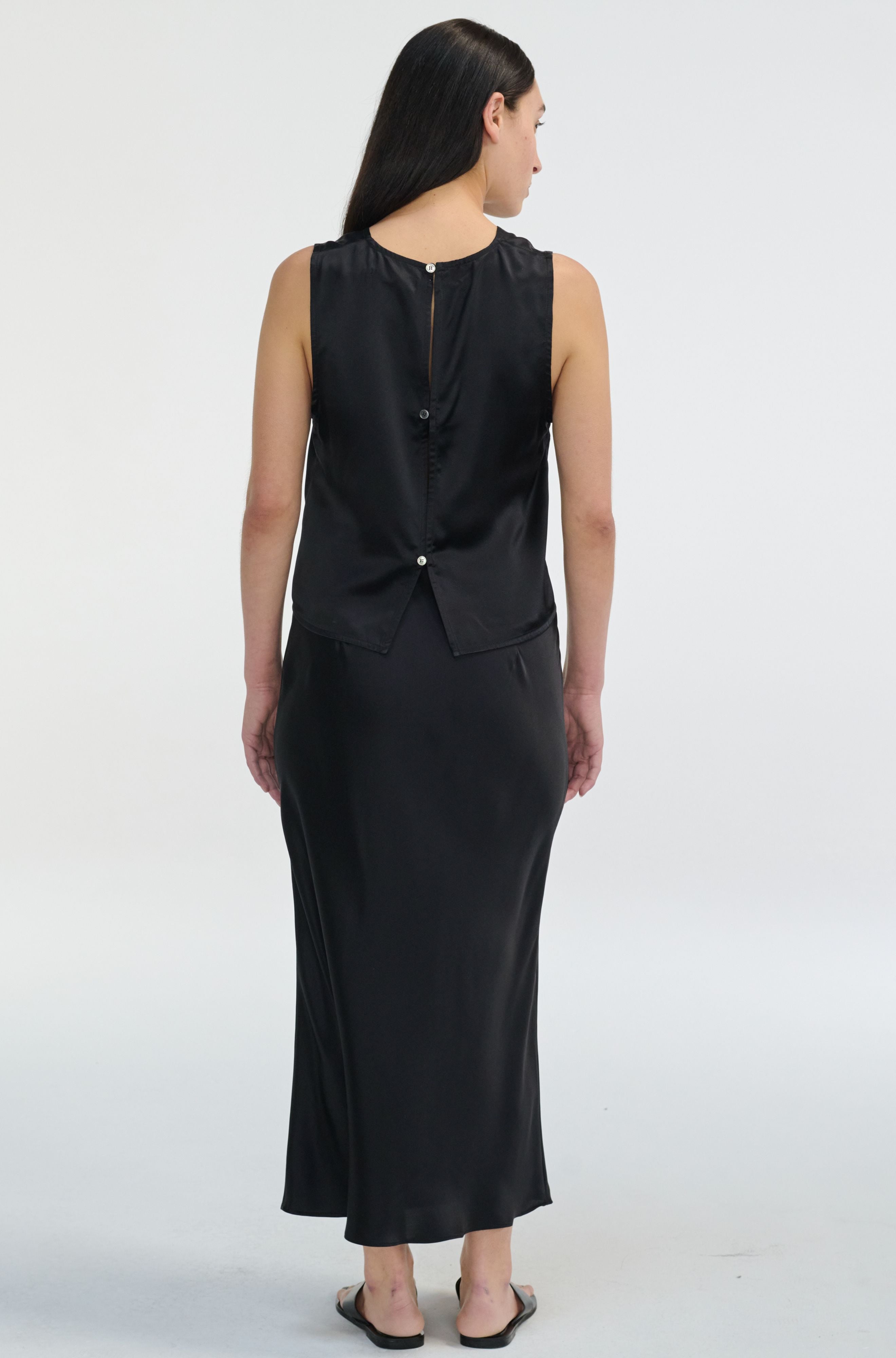 Woman wearing a black sleeveless silk top and skirt on a white background