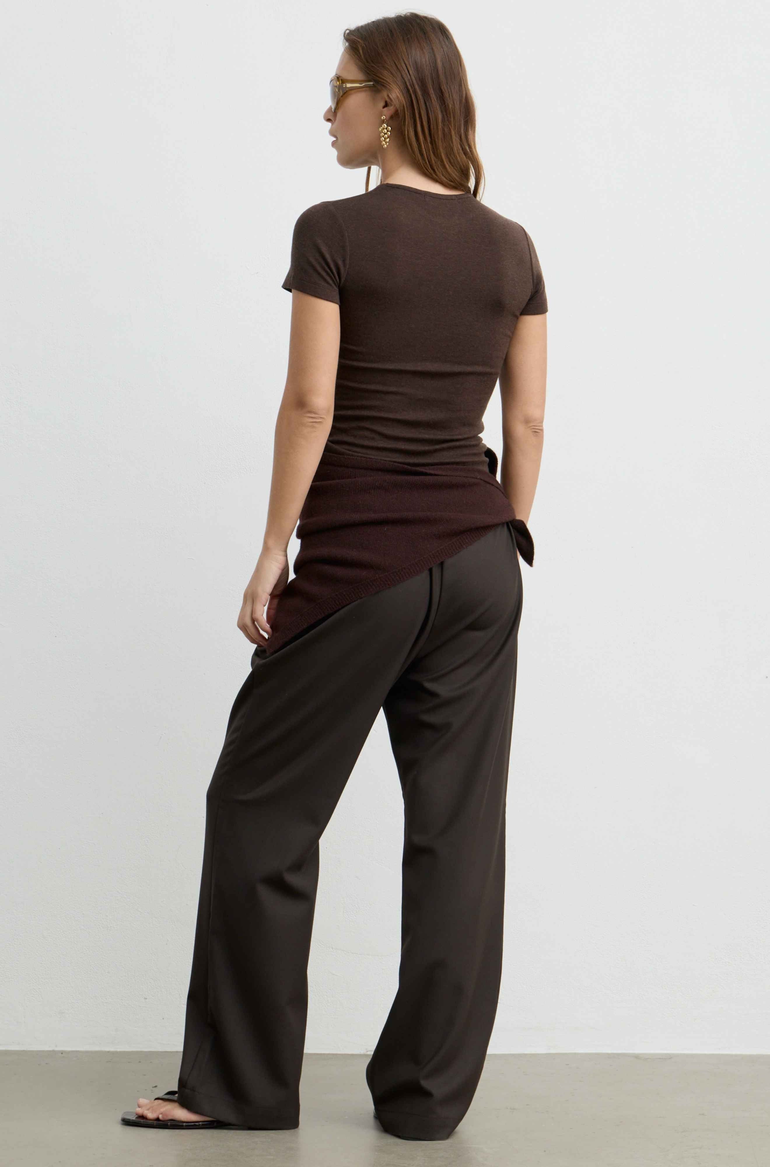 A woman shown from the back wearing a dark brown short-sleeve top and dark brown wide-leg pants, standing against a plain light gray studio background.