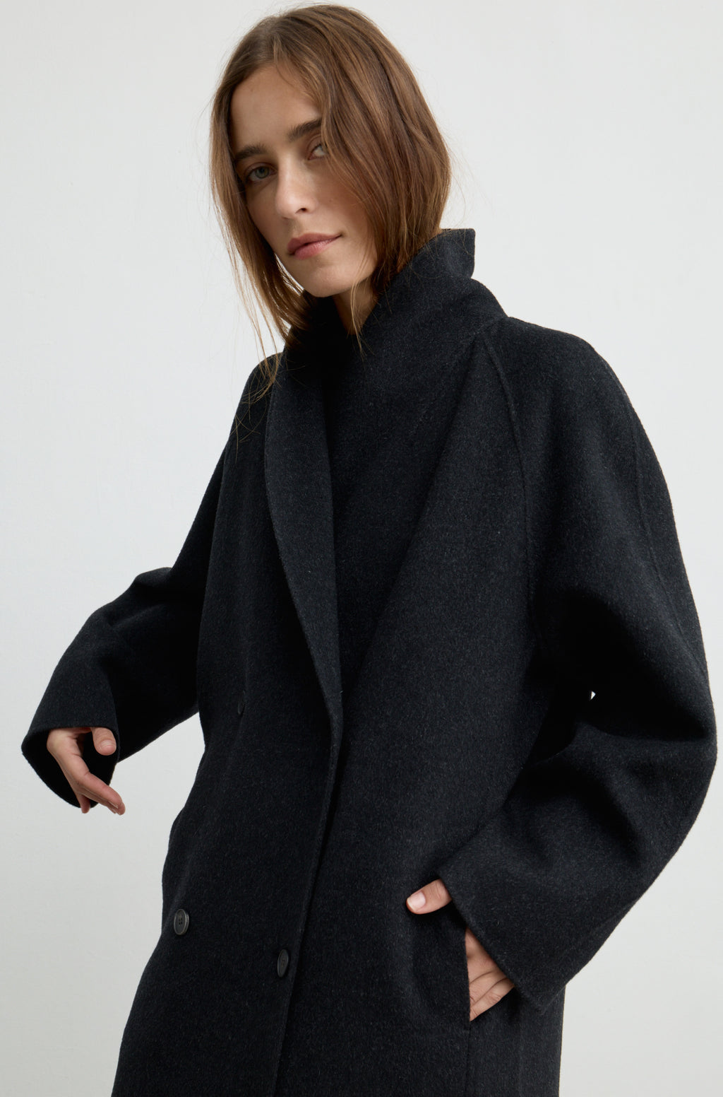 Woman wearing a dark grey button up coat against a light grey wall