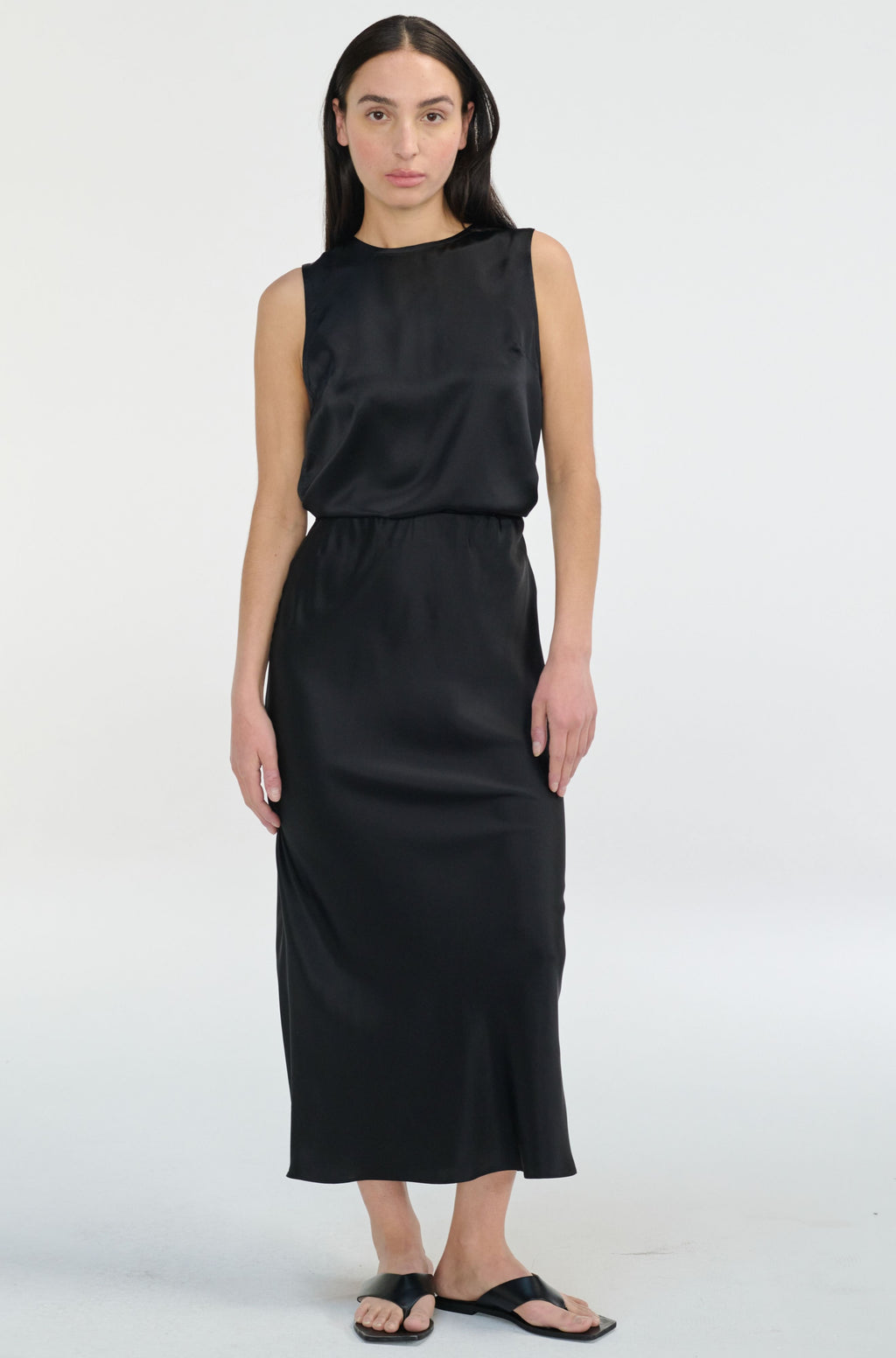 Woman wearing a black sleeveless silk top and skirt set on a white background