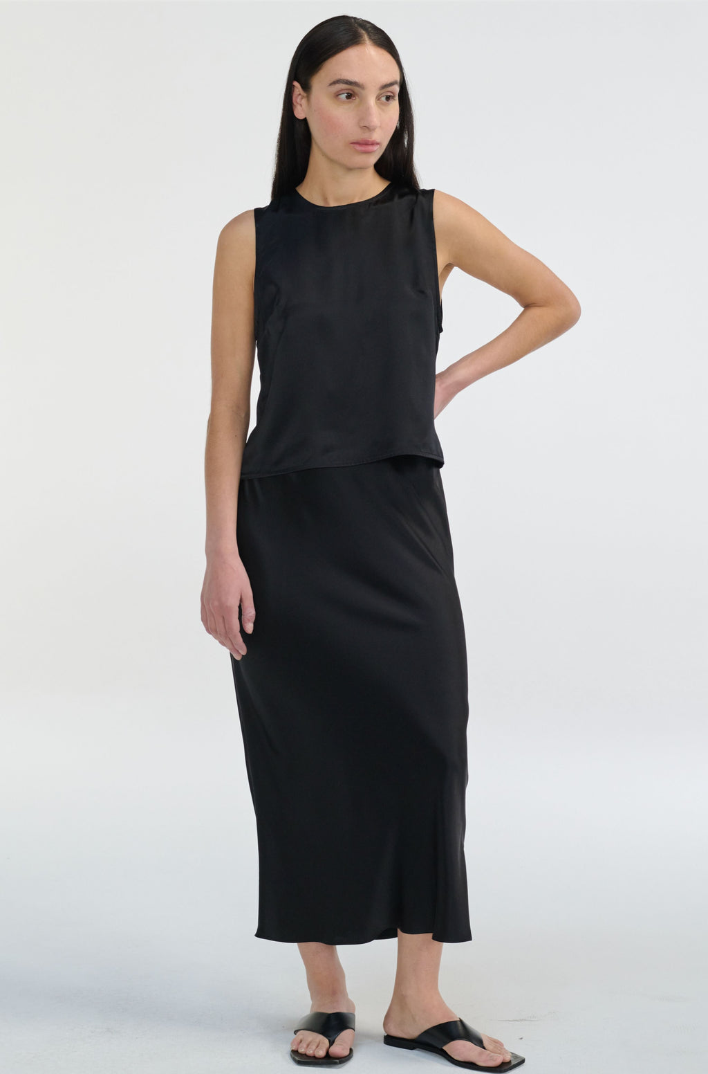 Woman wearing a black sleeveless silk top and skirt on a white background