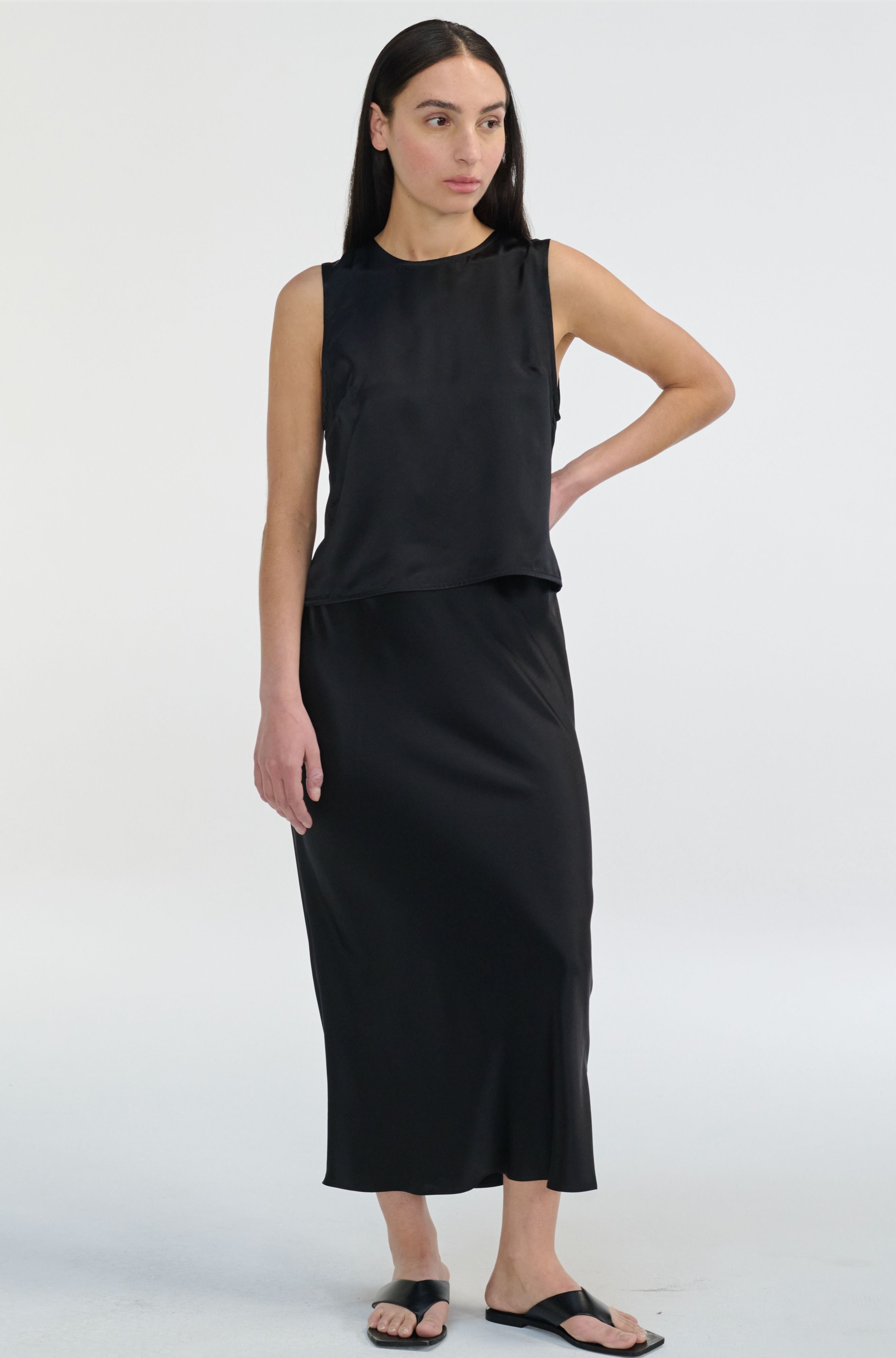 Woman wearing a black sleeveless silk top and skirt on a white background