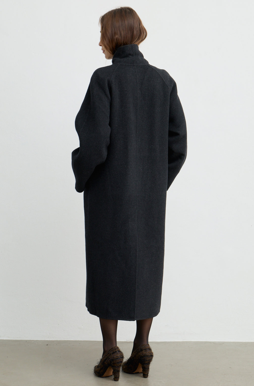Woman wearing a grey coat against a light grey wall