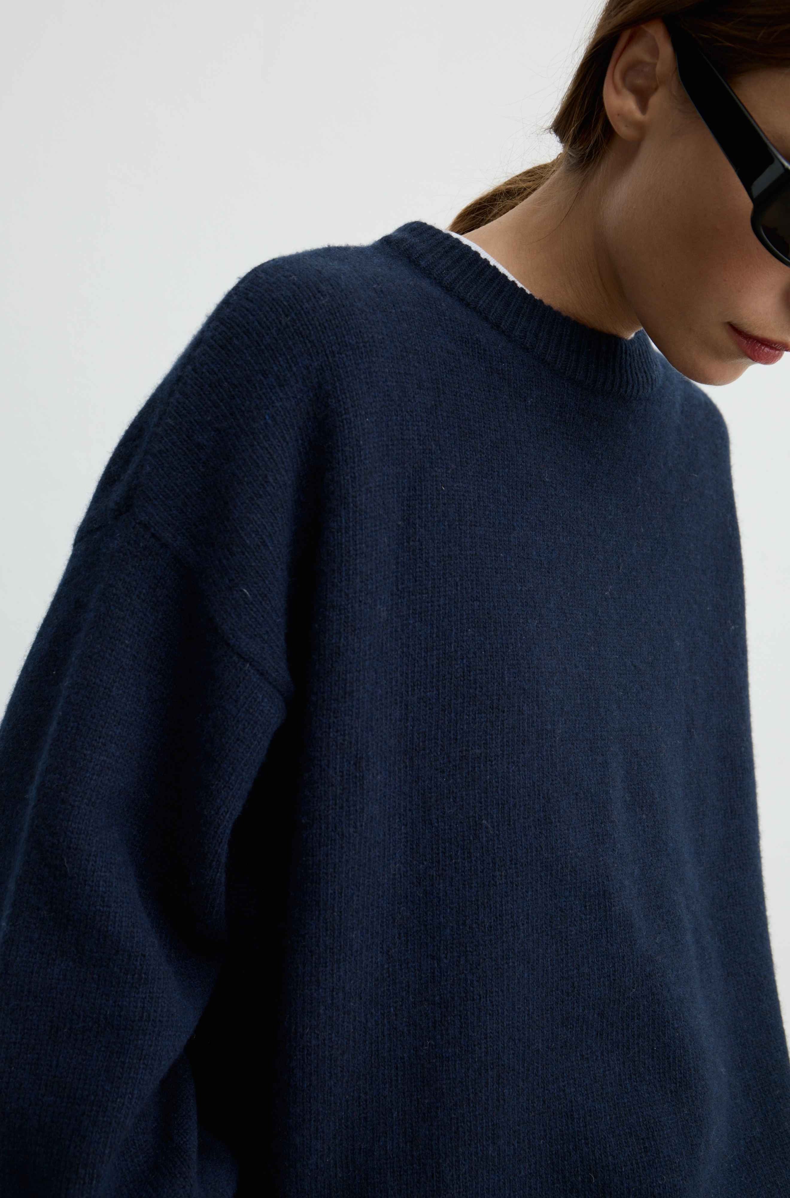 A close-up of a person wearing an oversized navy blue knit sweater against a plain light background.