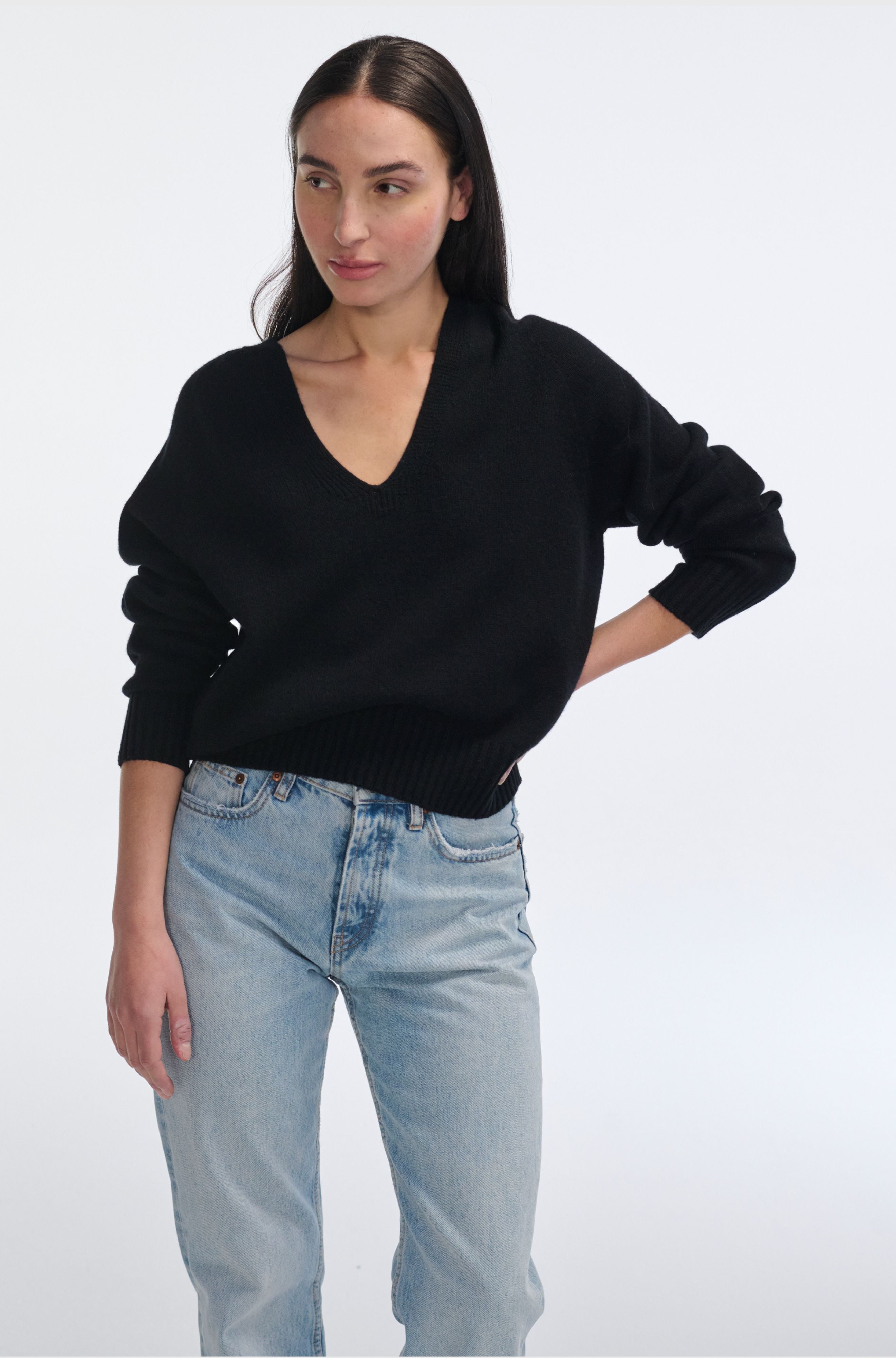 Woman wearing a black sweater and light blue jeans on a white background