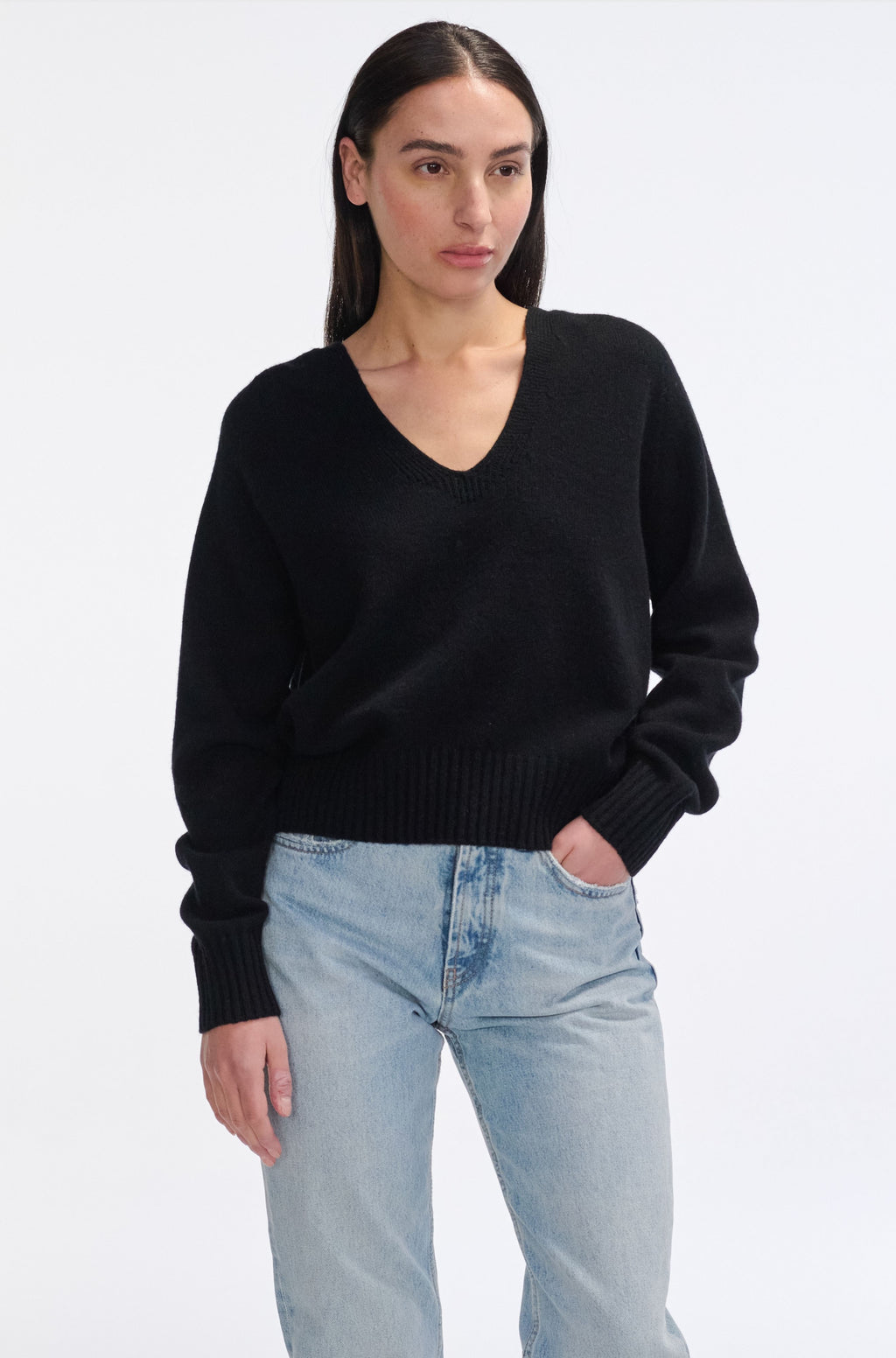 Woman wearing a black sweater and light blue jeans on a white background