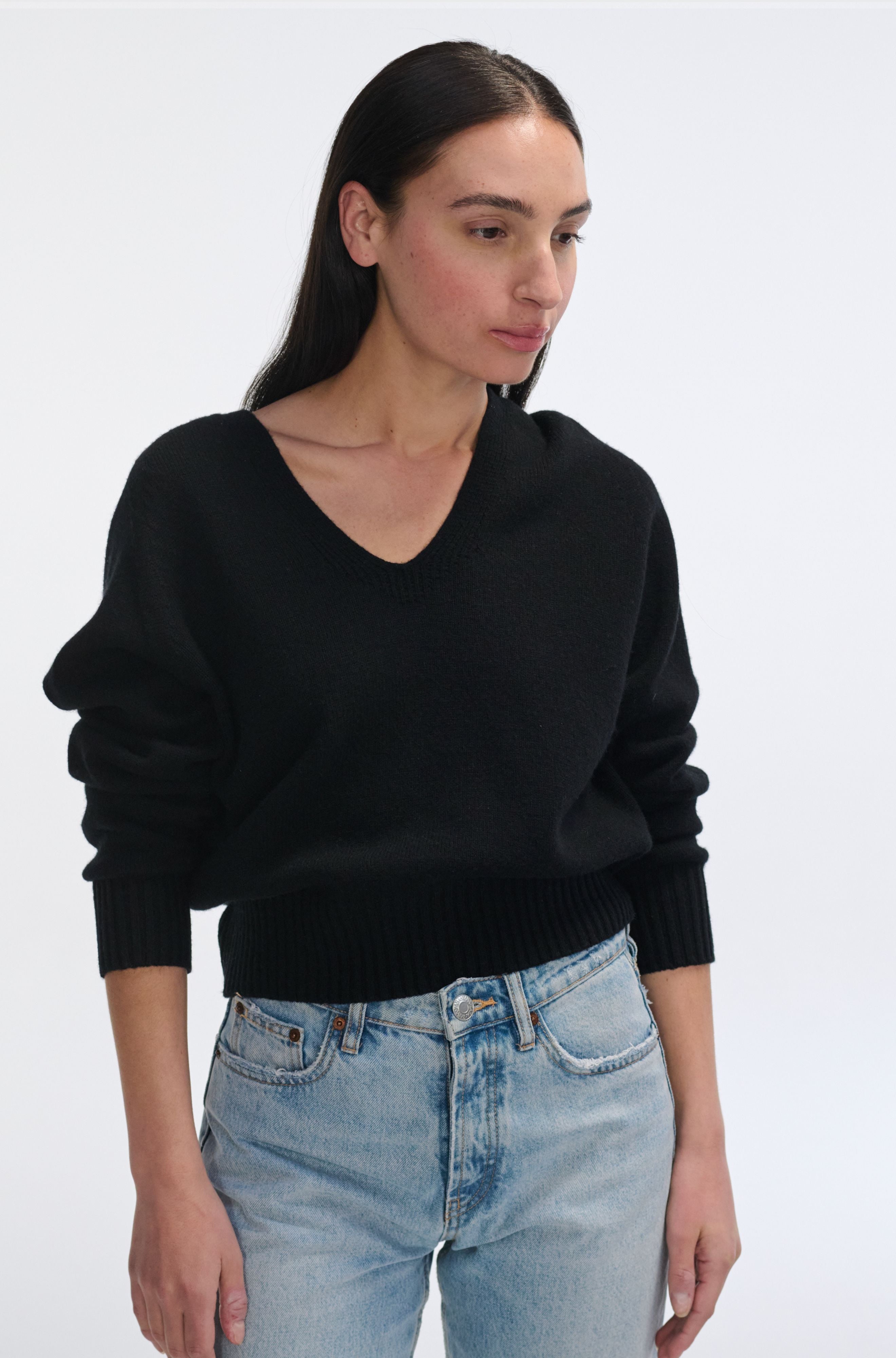Woman wearing a black sweater and blue jeans against a white background