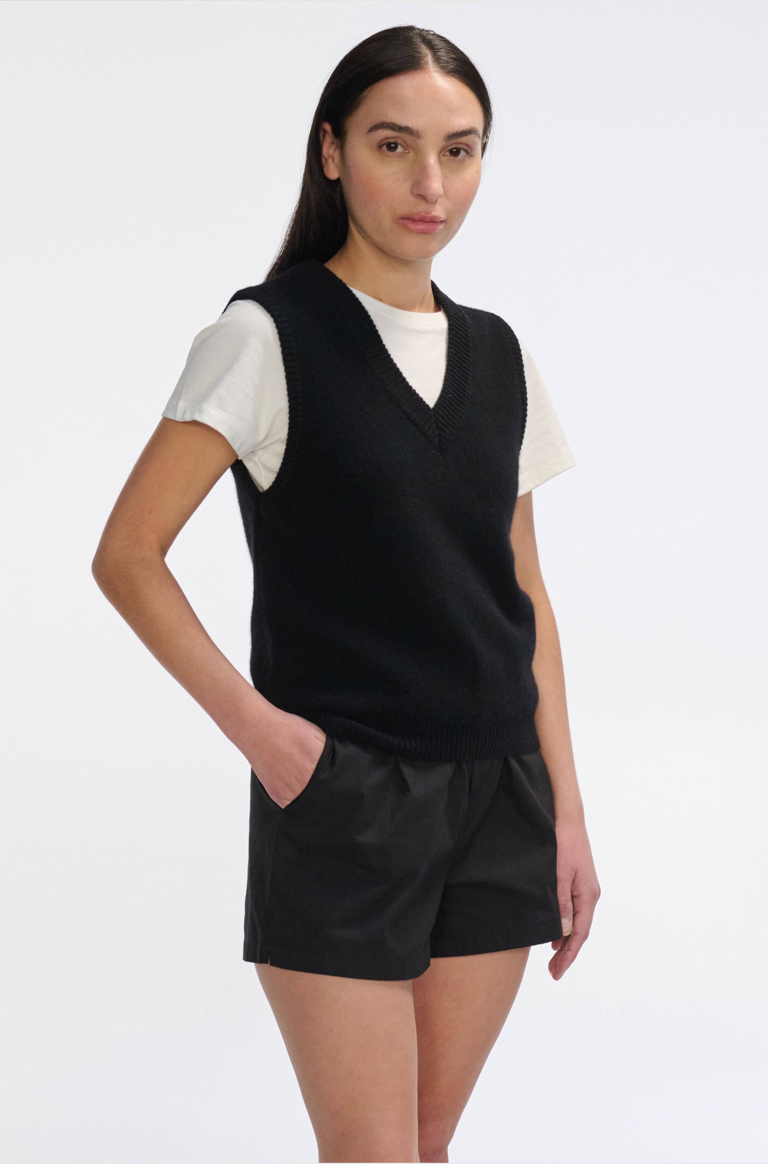 Woman wearing a black v neck knit top with black shorts against a white background