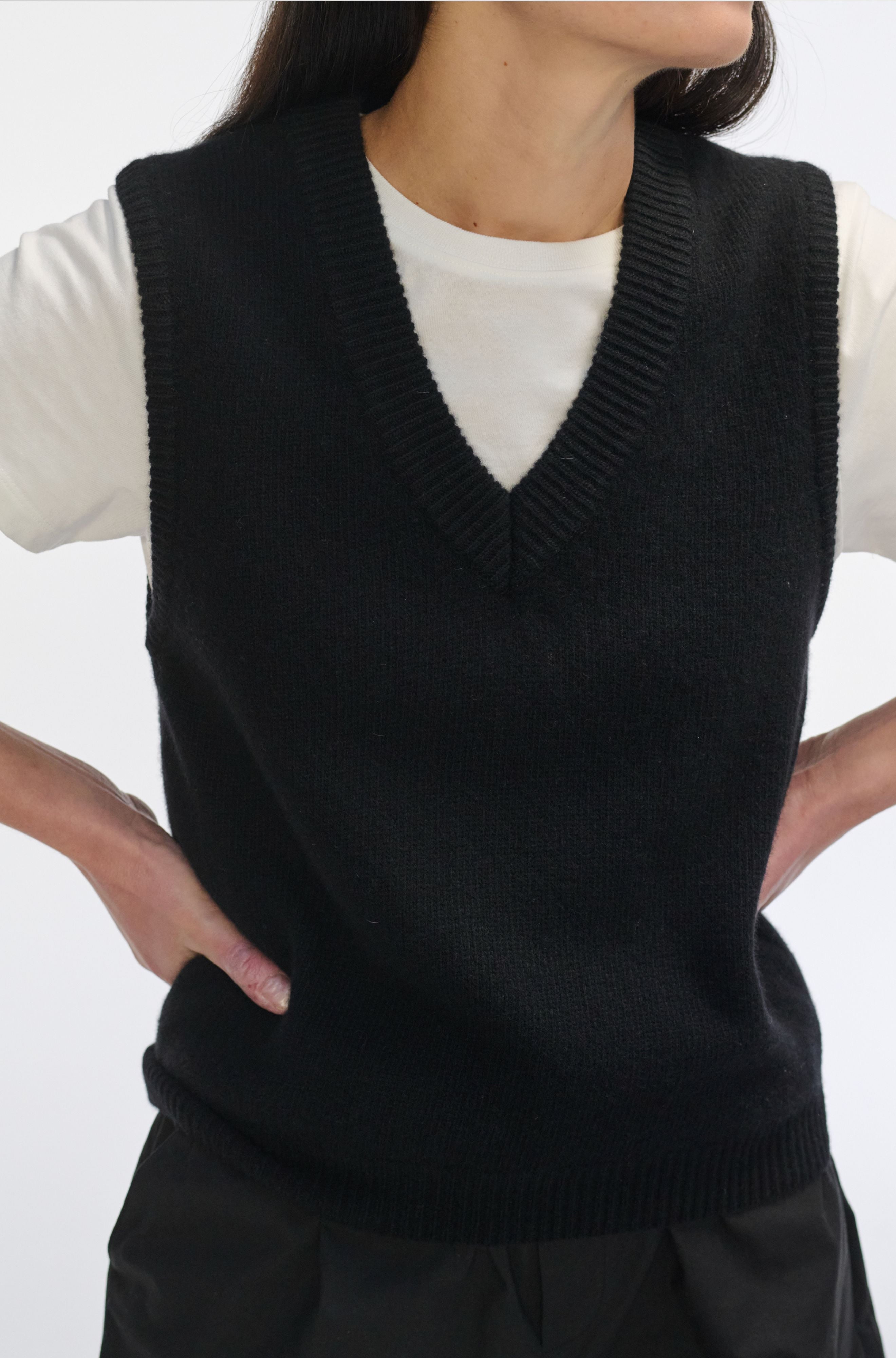 Person wearing a black knitted vest over a white shirt on a white background
