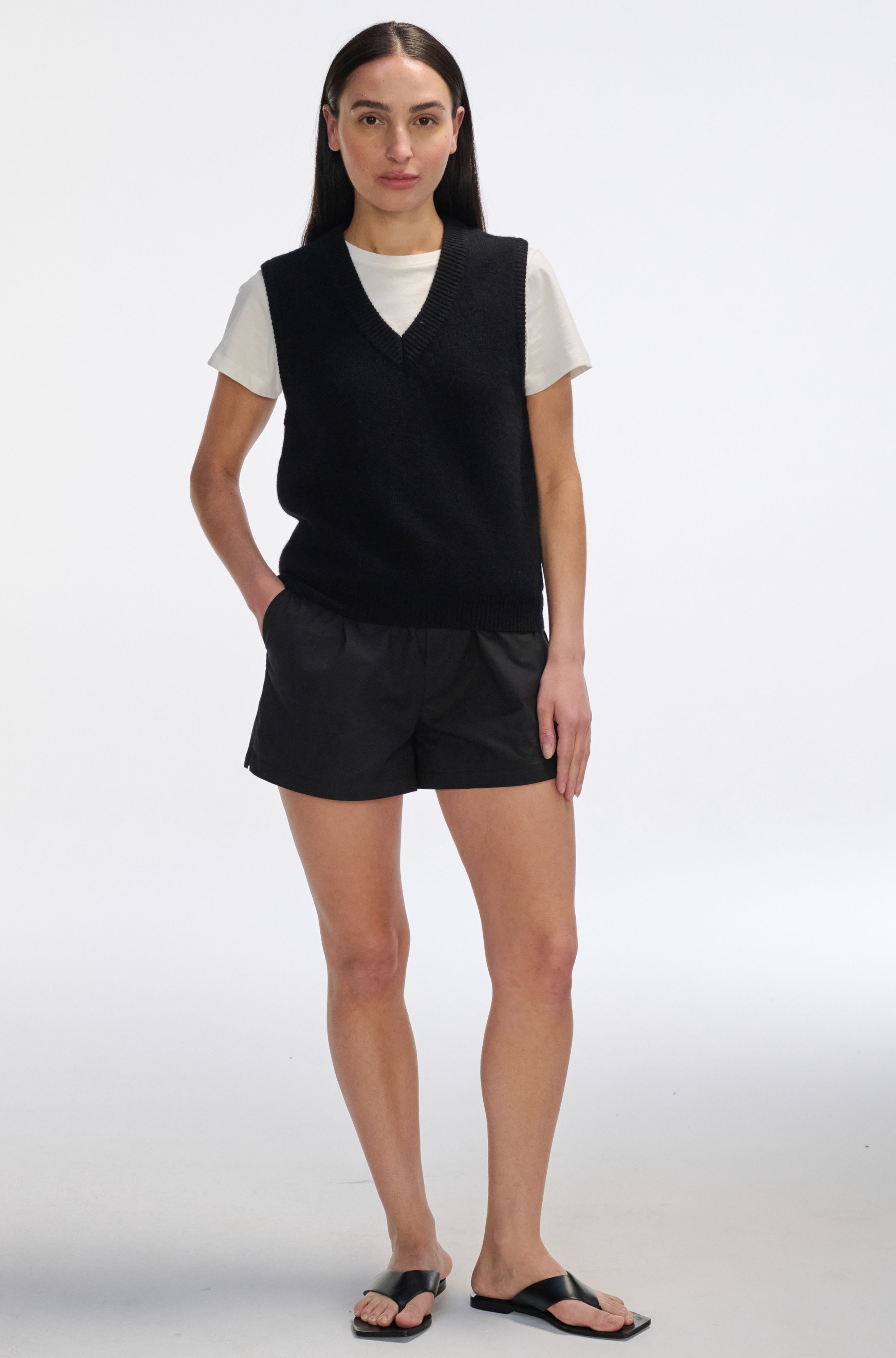 Woman wearing a black vest over a white shirt and black shorts on a white background
